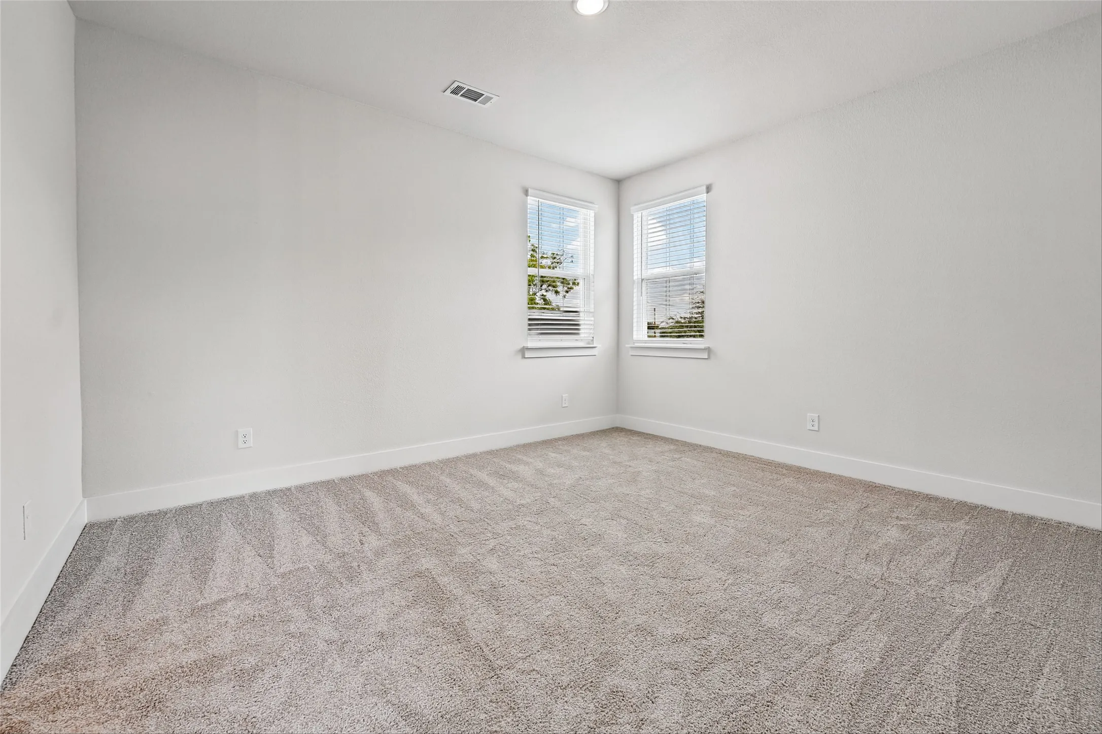 Recessed ceiling lighting, two windows with blinds, light-toned carpeting, and white wall finishes