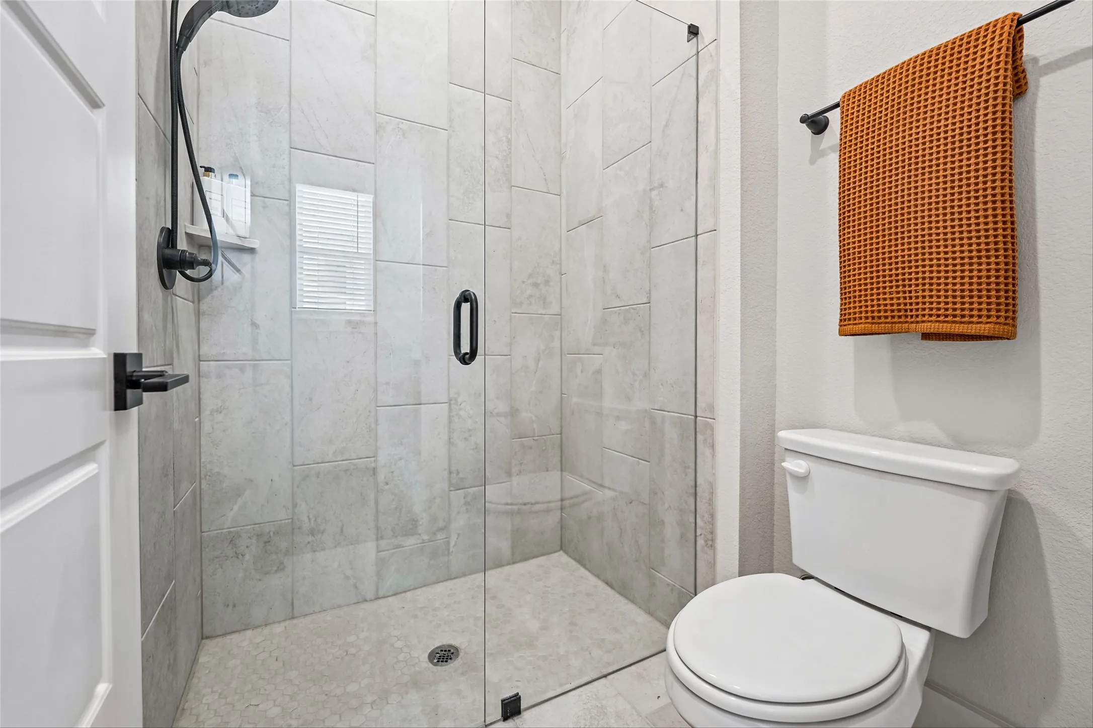 Glass-enclosed shower with subway tile surround, matte black shower fixtures, and mosaic tile flooring