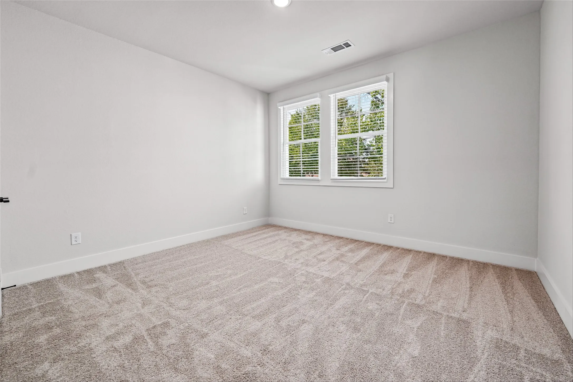 Carpeted flooring, white walls, two windows with blinds, and recessed lighting