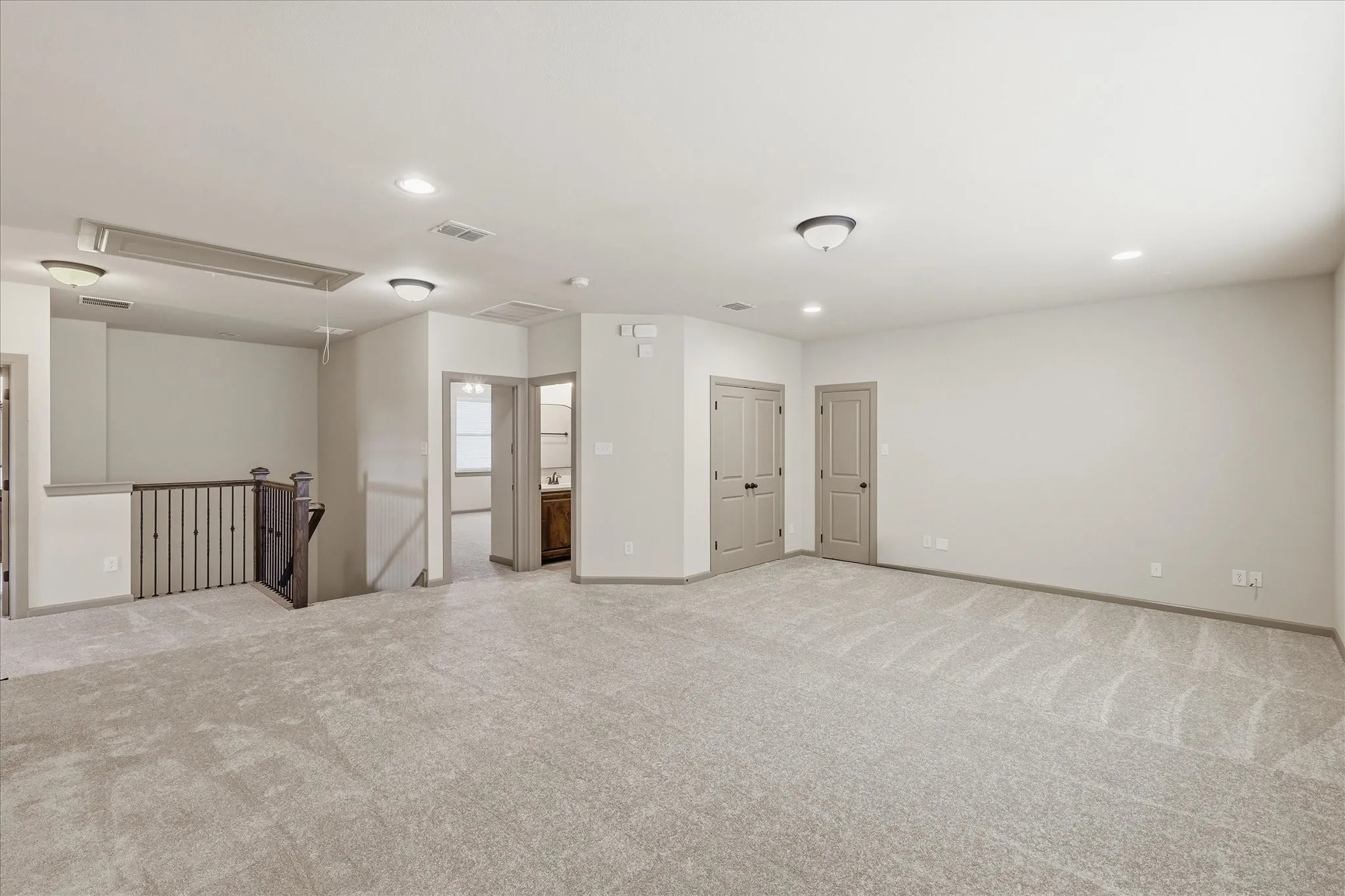 Spacious carpeted room featuring recessed lighting, a dark wood-finish staircase with wrought iron balusters, and multiple interior doors with dark hardware