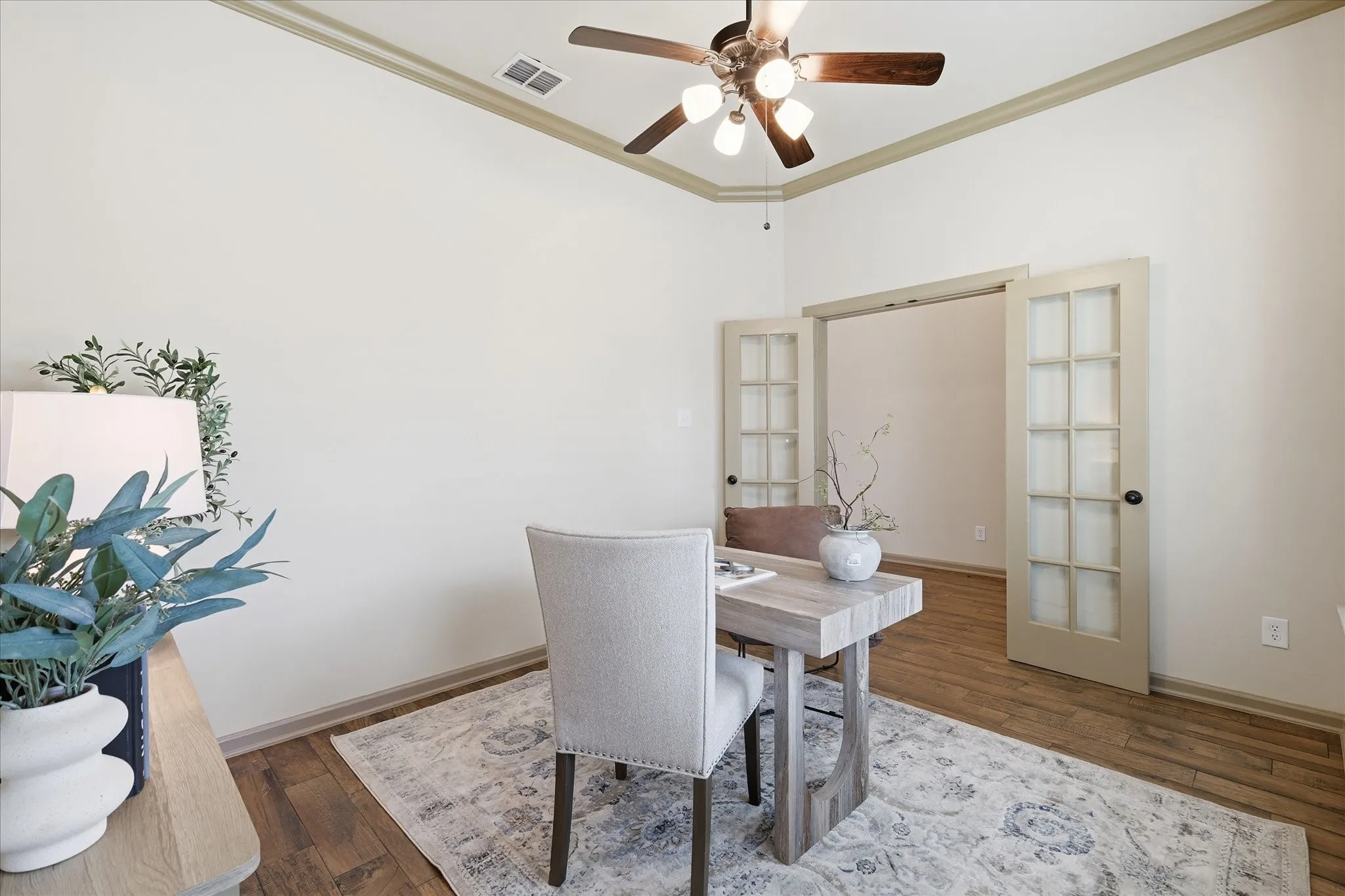Room featuring warm wood-finish flooring, French doors with grid-pane glass, crown molding, and a ceiling fan with integrated lighting