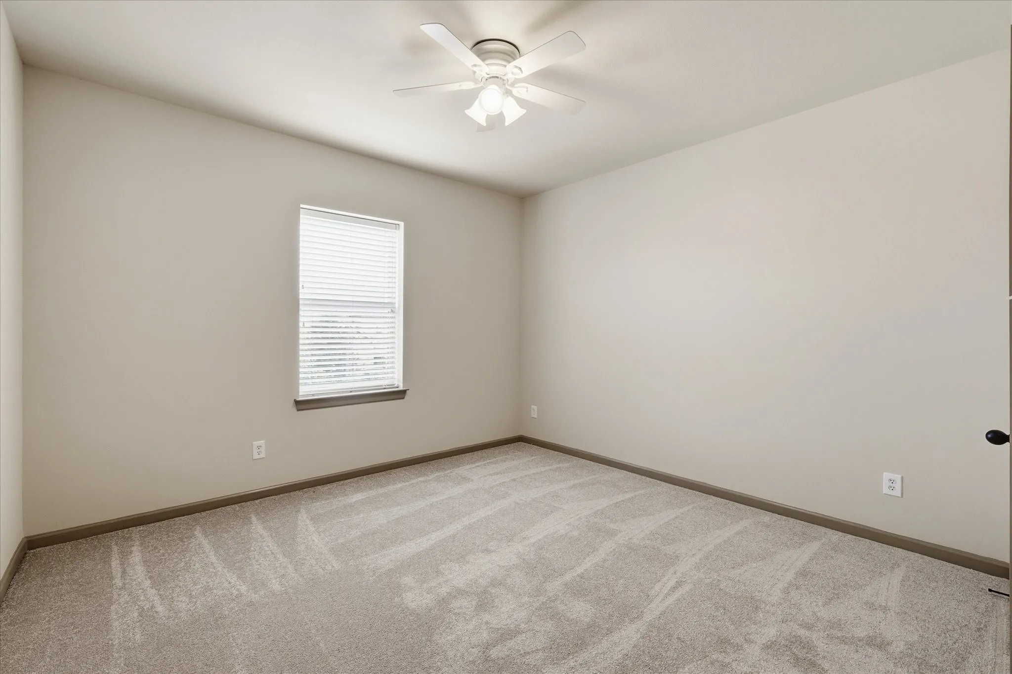 Neutral-toned room featuring a single window with blinds, light-colored carpeting, and a ceiling fan with integrated lighting