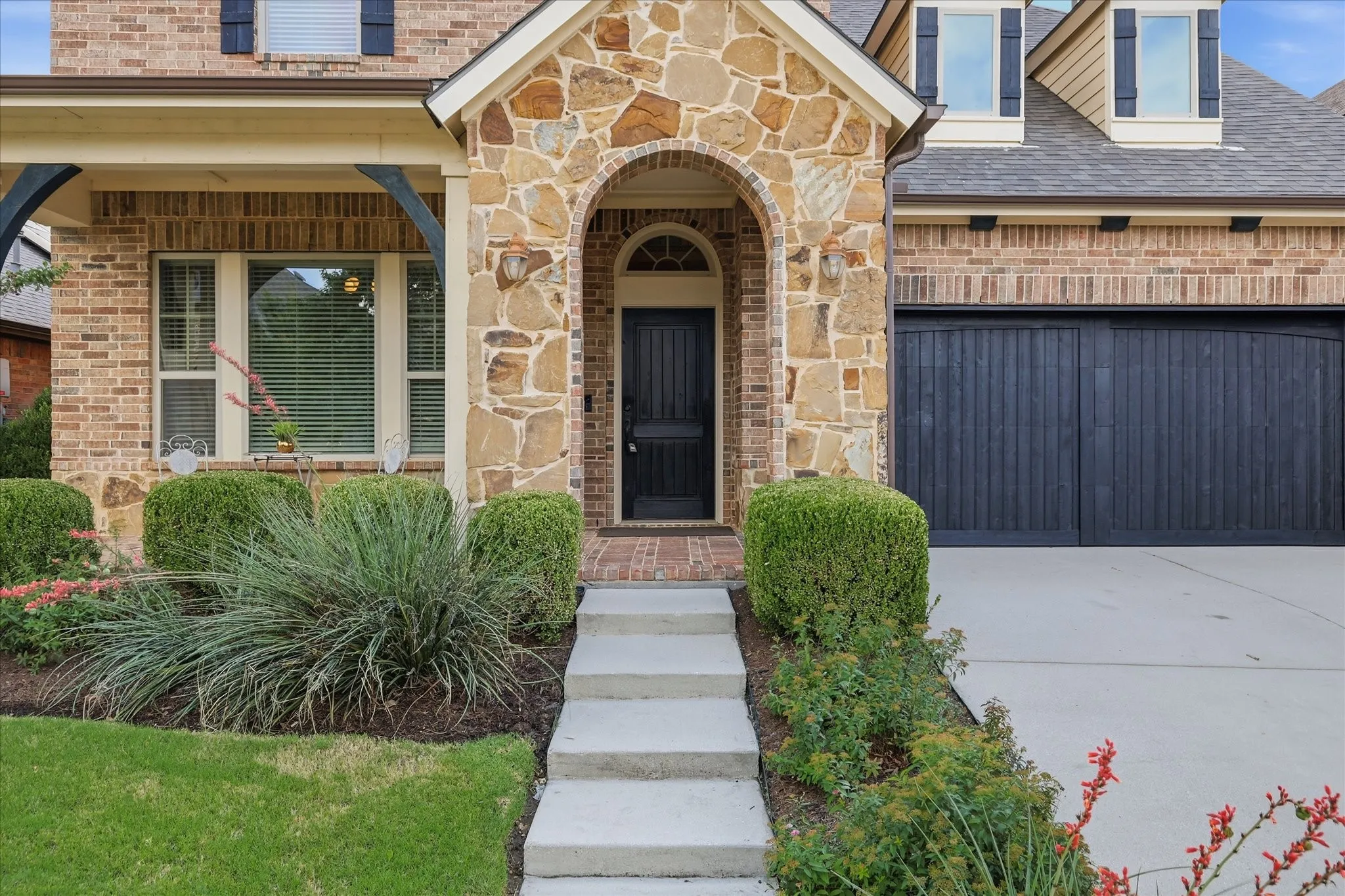 Brick and stone facade featuring an arched entryway, a dark paneled front door, and a dark paneled garage door