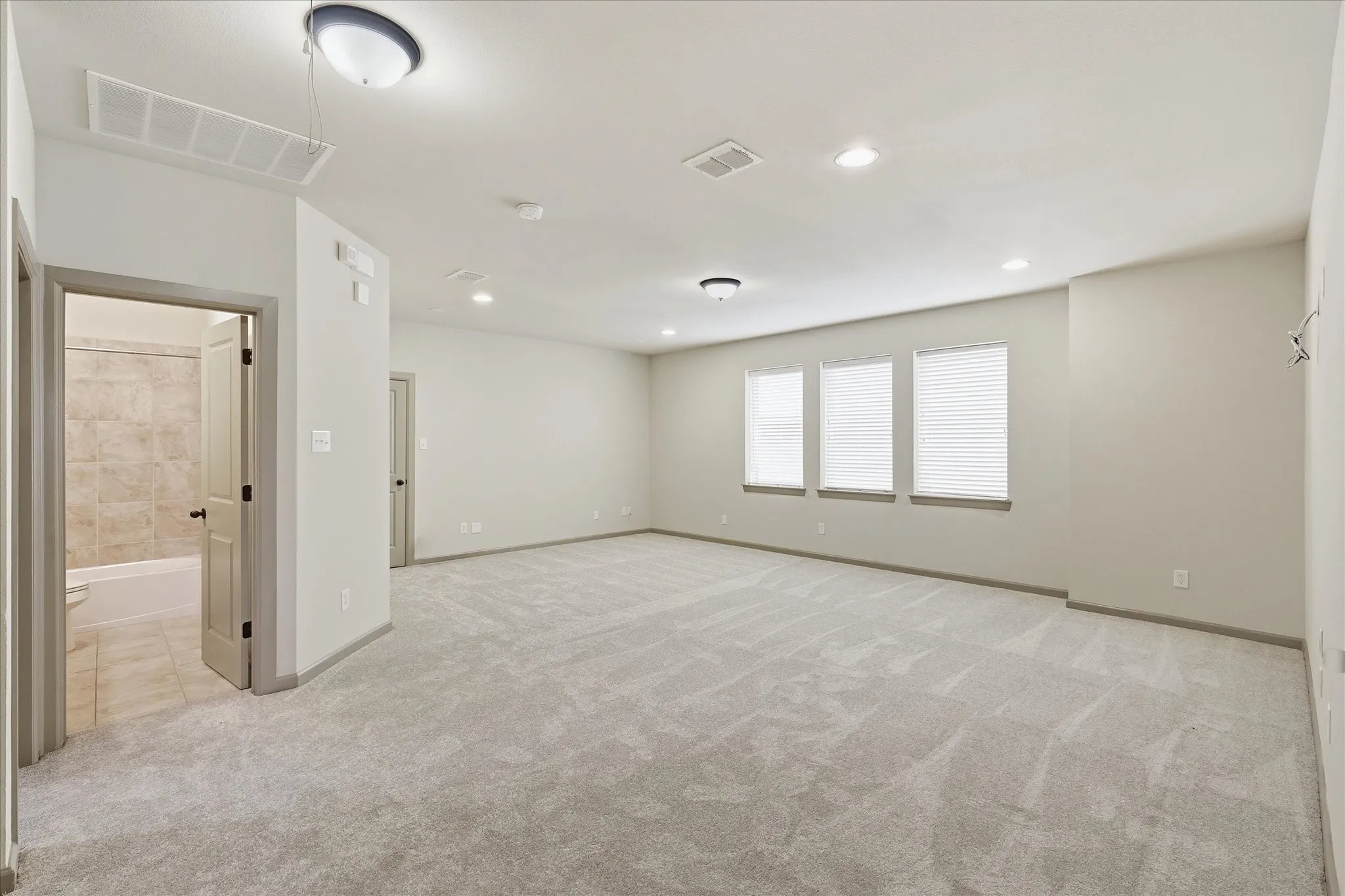 Spacious room featuring light-colored carpeting, three windows with blinds, recessed lighting, and a neutral wall palette