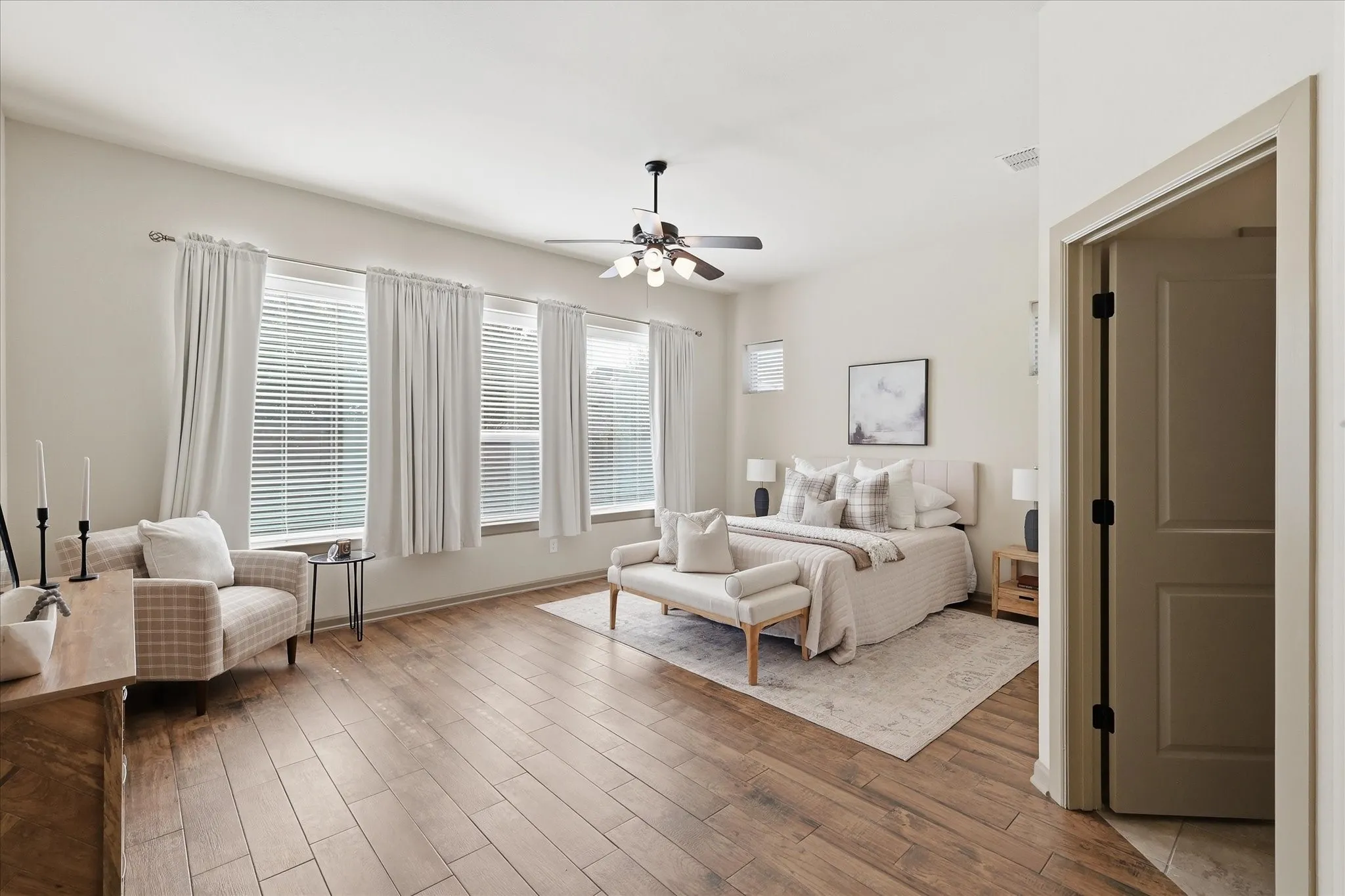 Spacious room featuring wood-finish tile flooring, multiple windows with blinds and curtains, and a ceiling fan with integrated lighting