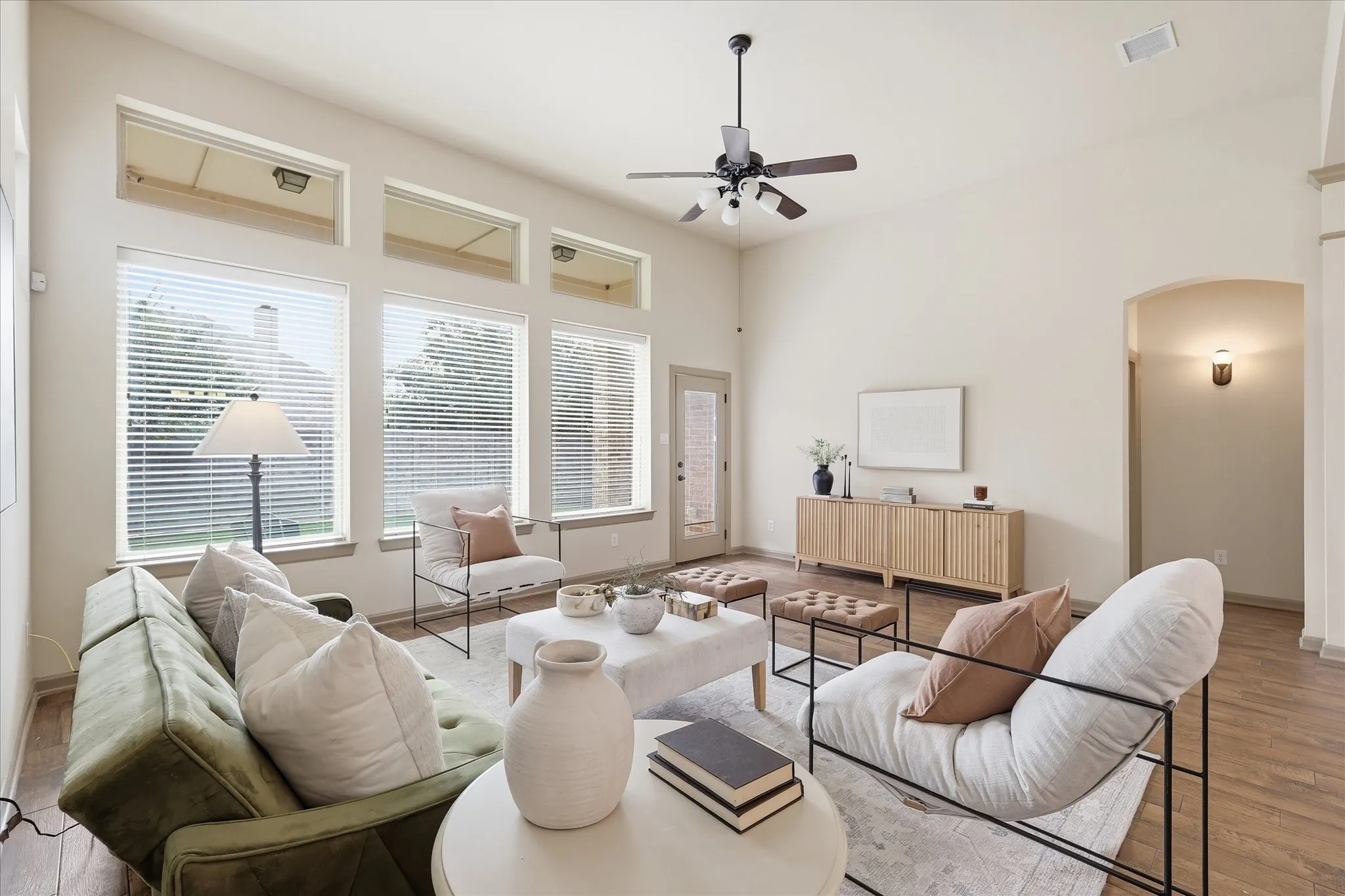 Vaulted ceiling living area featuring a wall of windows looking into the back yard, wood-like tile flooring and an arched doorway leading to the primary bedroom