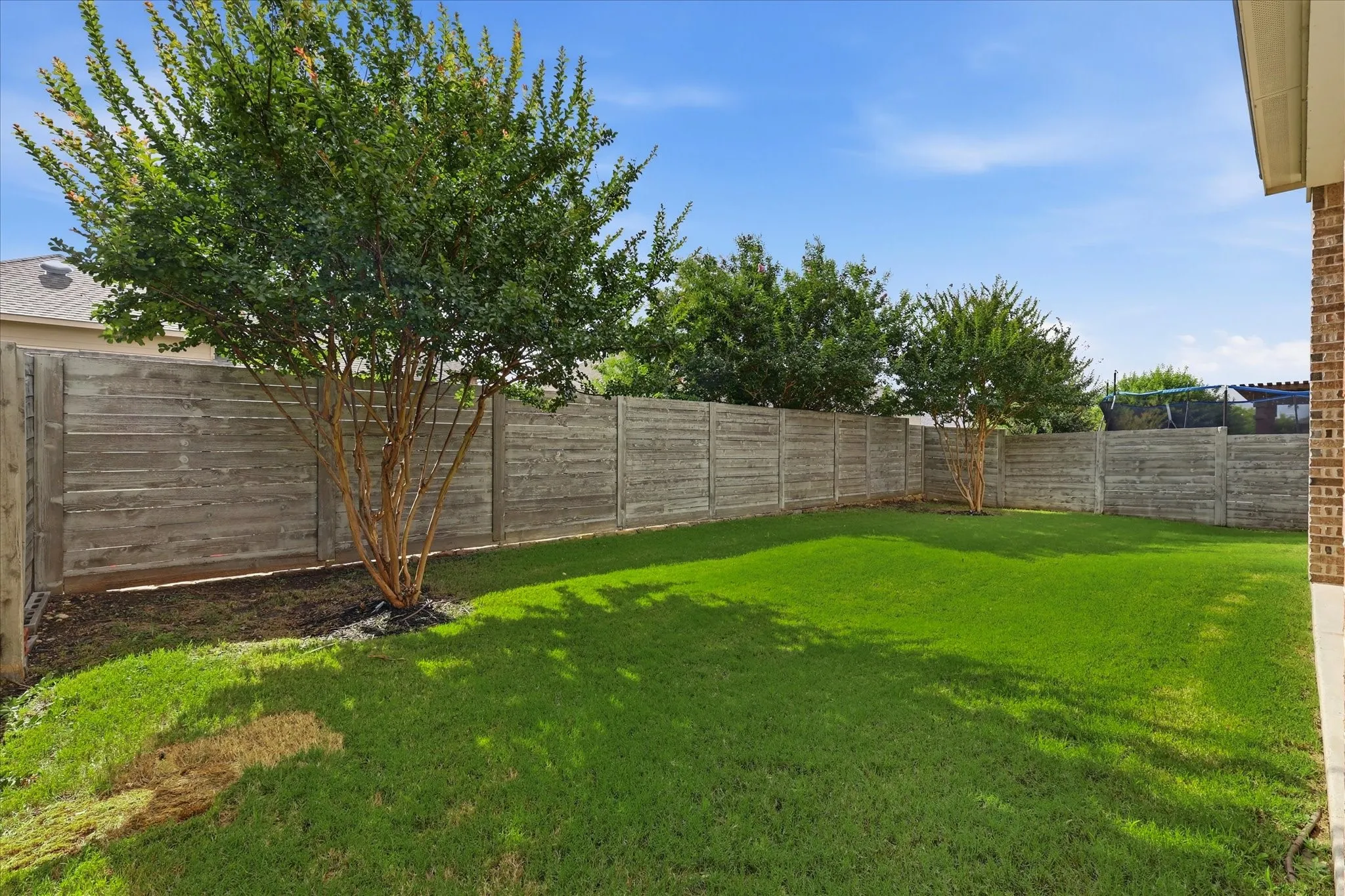 Private backyard featuring a horizontal plank fence, mature trees, and a spacious lawn