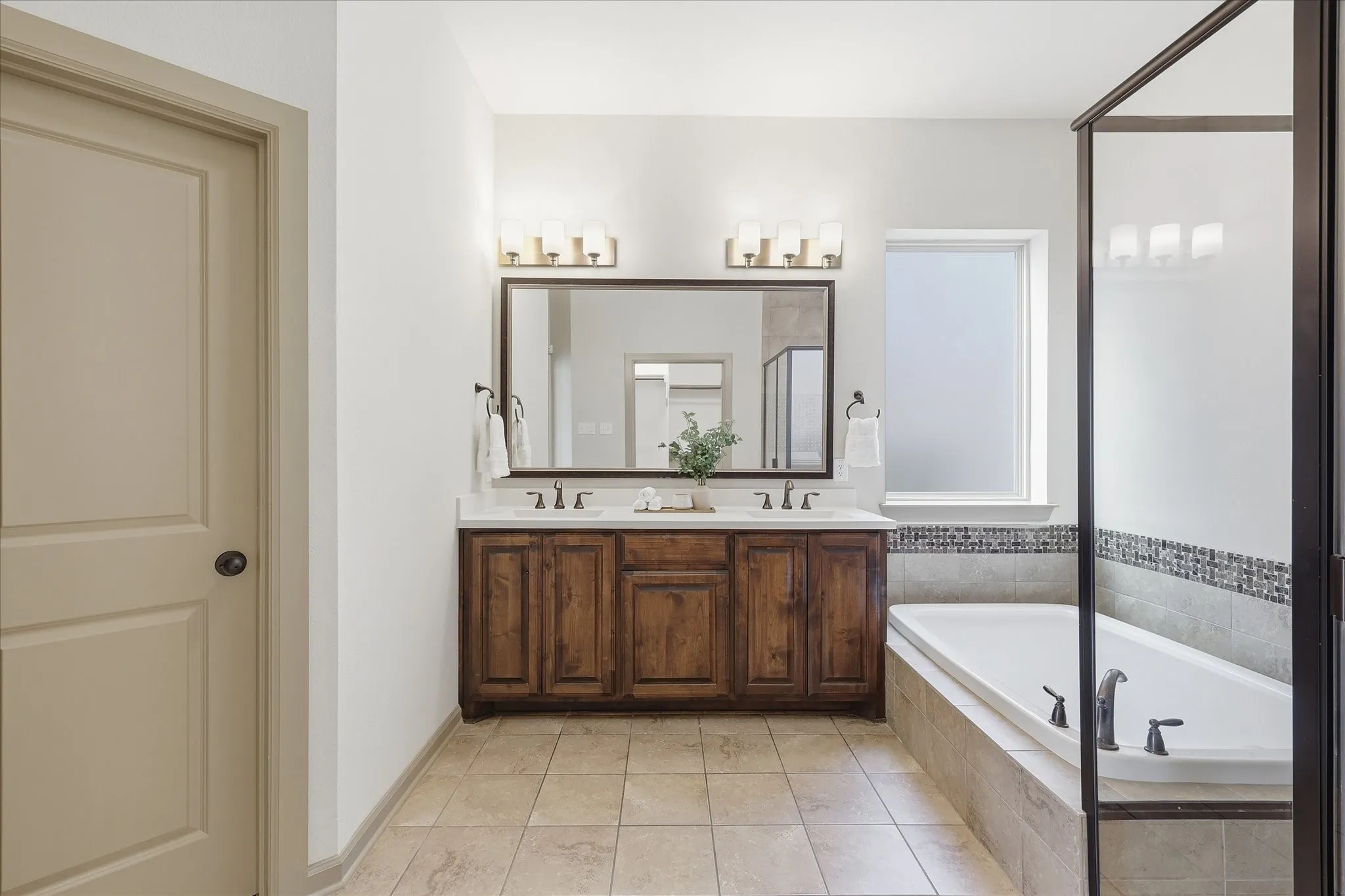 Dual vanity with wood-finish cabinetry, a large framed mirror, and two three-light fixtures