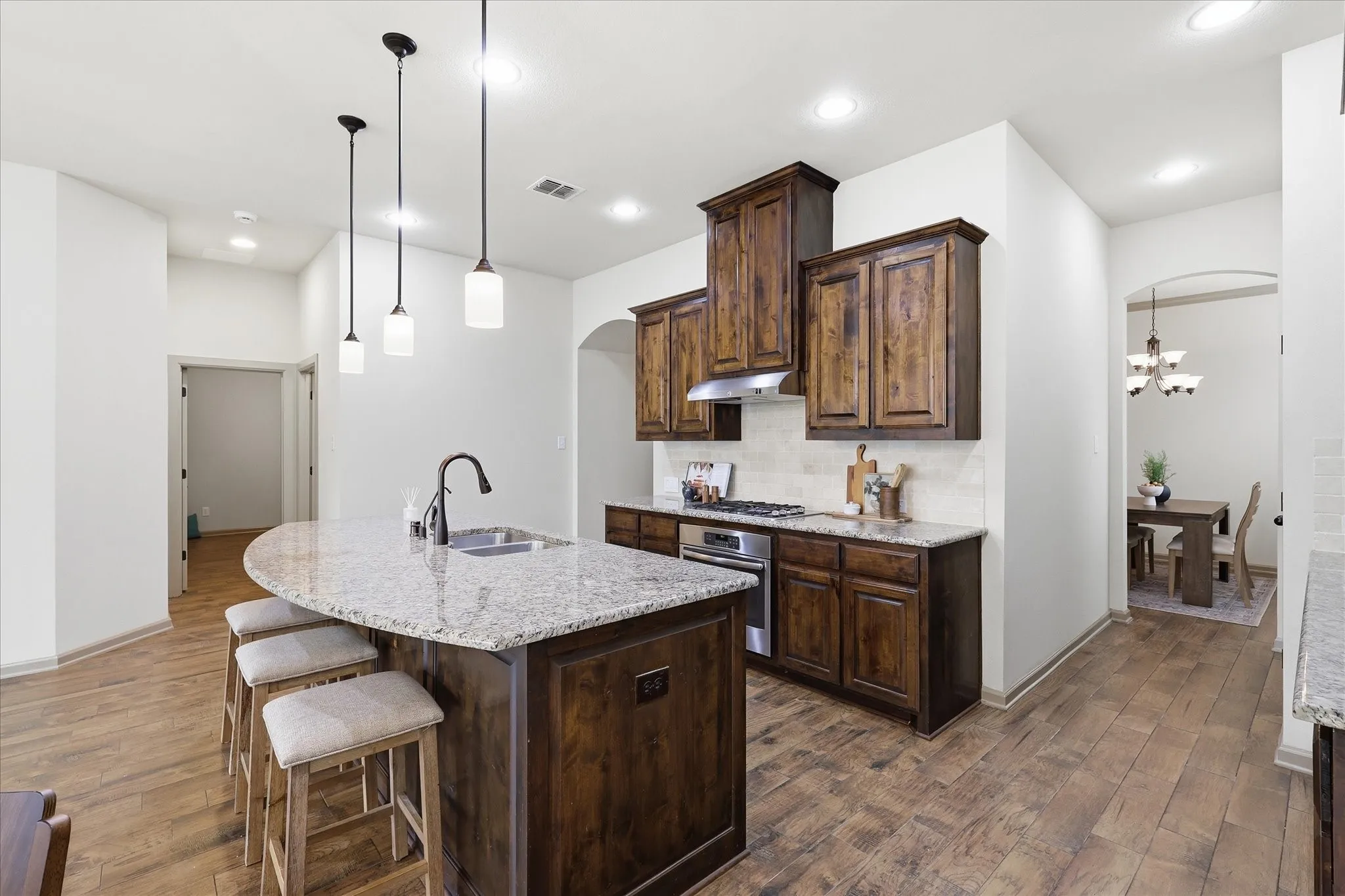 Island with sink and pendant lighting. Gas cooktop and dark wood cabinets