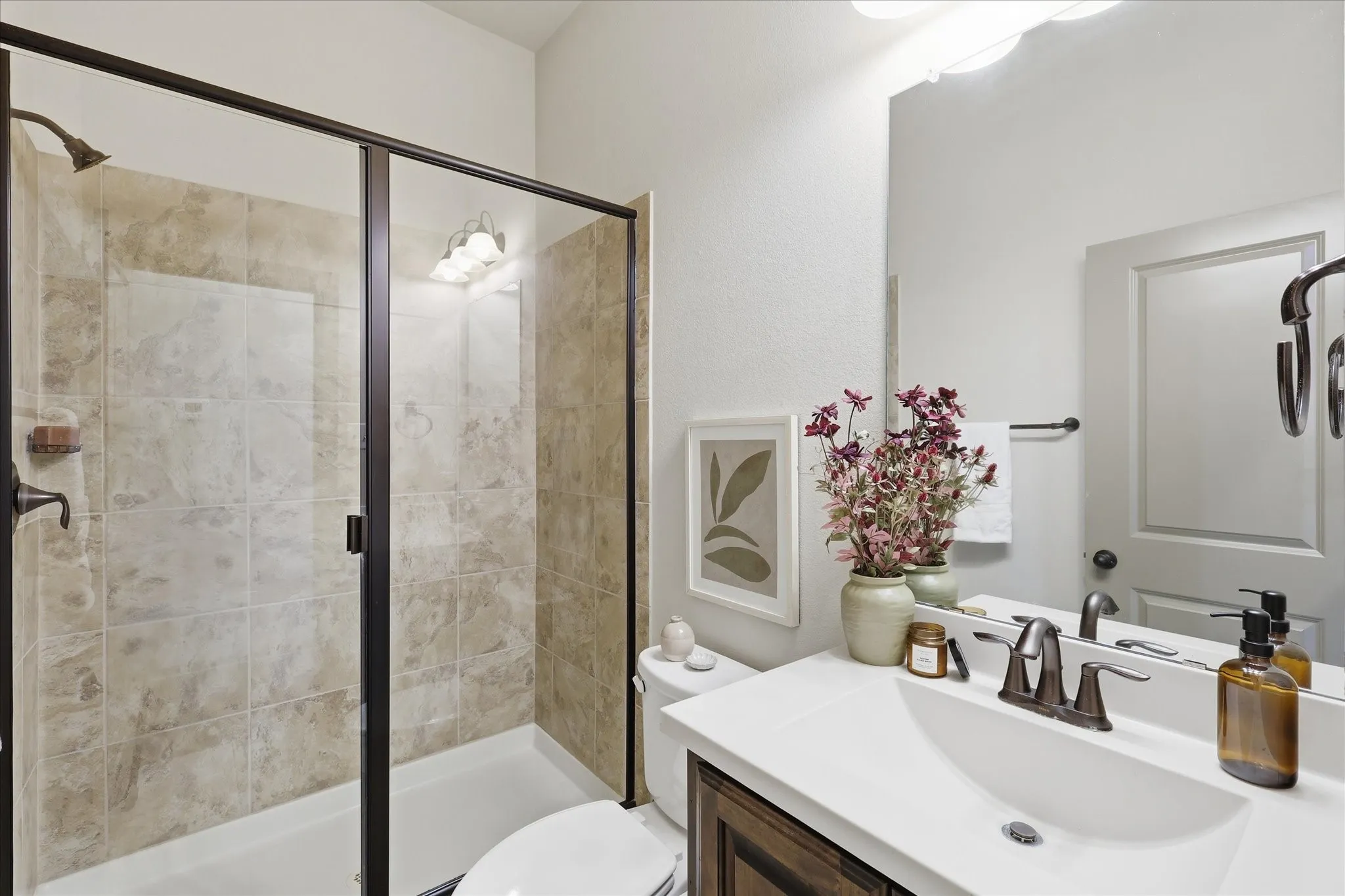 Downstairs bathroom has a shower with clear glass enclosure and bronze-finish hardware, featuring neutral-toned tiled walls and a white tub