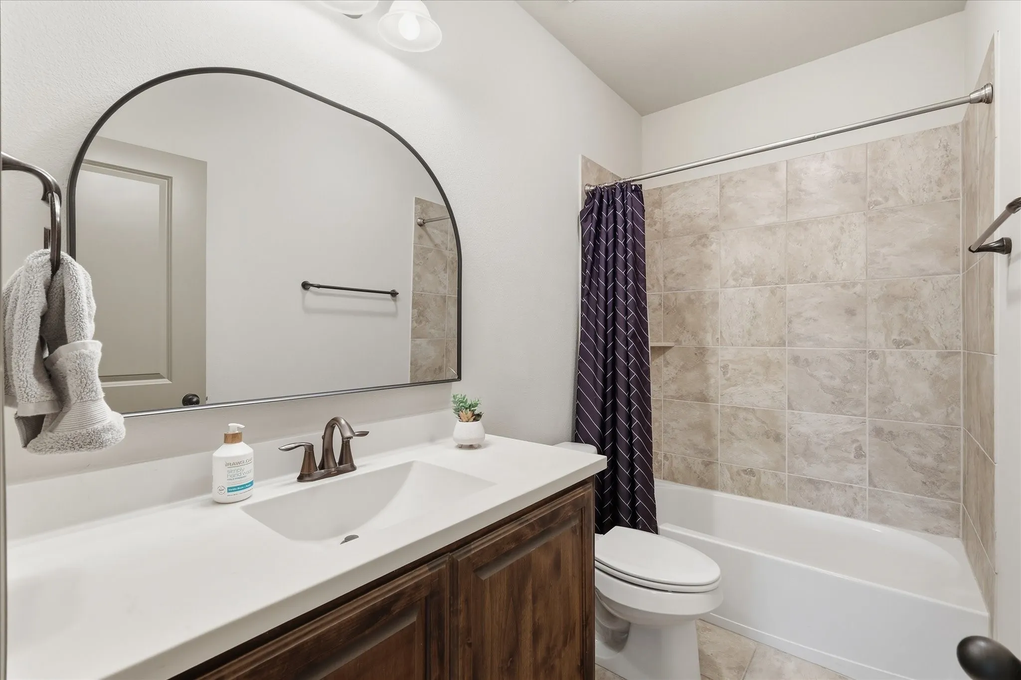 Bathroom featuring a dark wood-finish vanity with a white countertop, a bronze-finish faucet, and an arched-frame mirror