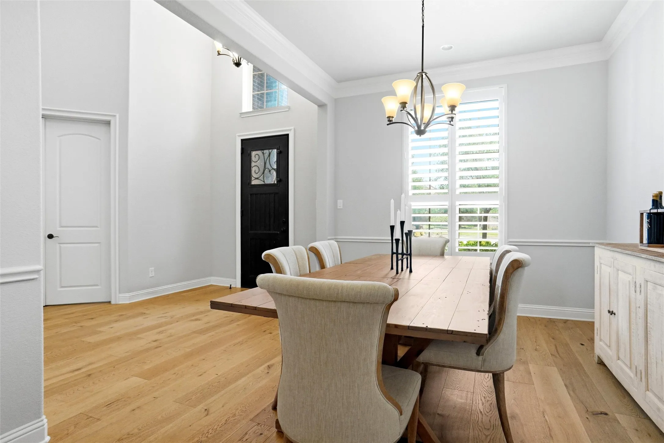 Dining area featuring light wood-finish flooring, a contemporary chandelier, and a window with plantation shutters