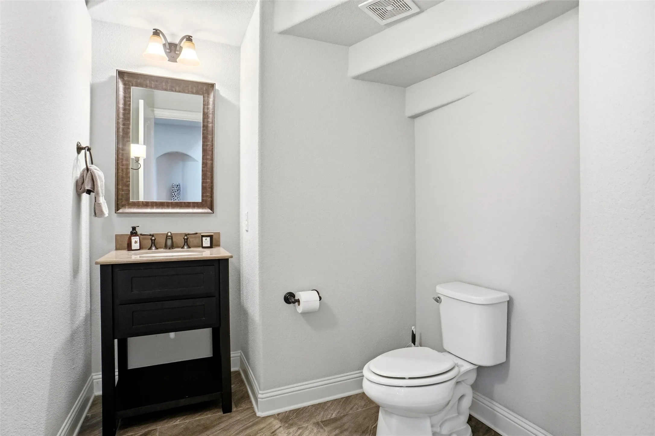 Powder room featuring a single-sink vanity with a dark wood-finish cabinet, a light-toned countertop, and a framed mirror