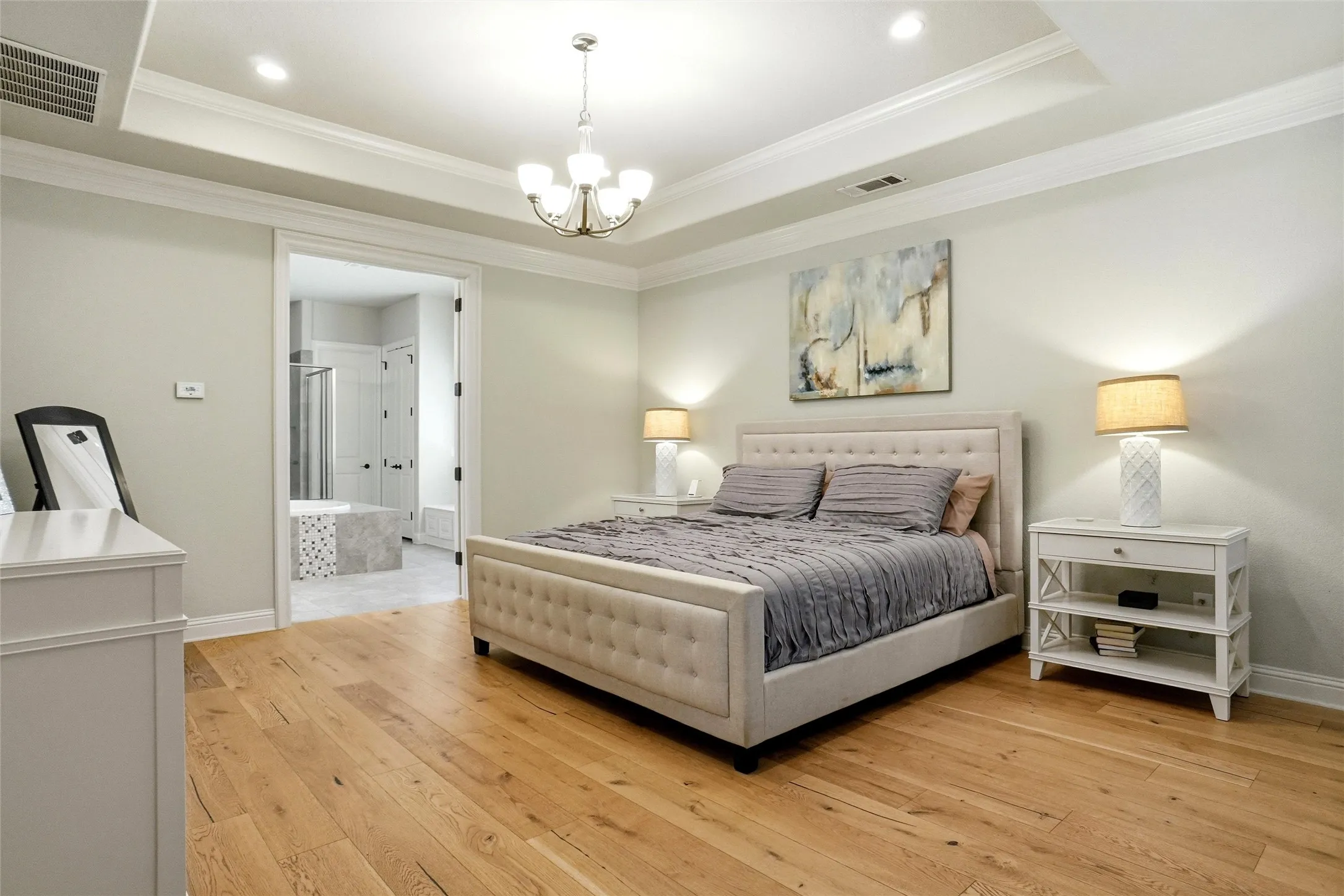 Hardwood flooring throughout the room with a tray ceiling and crown molding