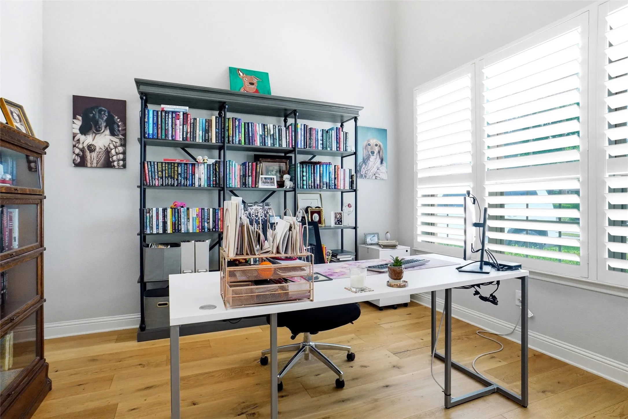 Spacious room featuring light wood-finish flooring, tall windows with plantation shutters, a substantial built-in shelving unit, and high ceilings