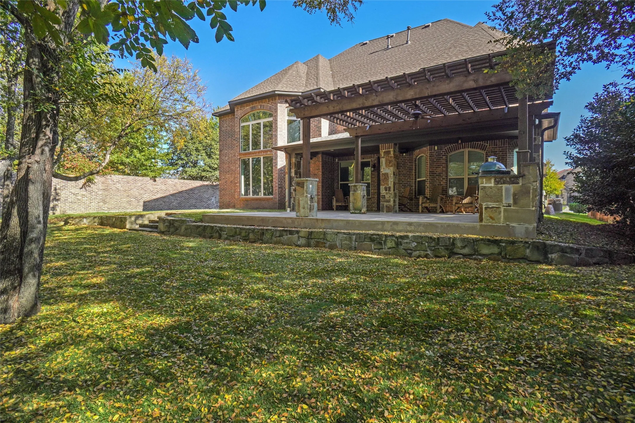 Expansive backyard featuring a stone retaining wall, mature trees, and a multi-level patio with a wooden pergola