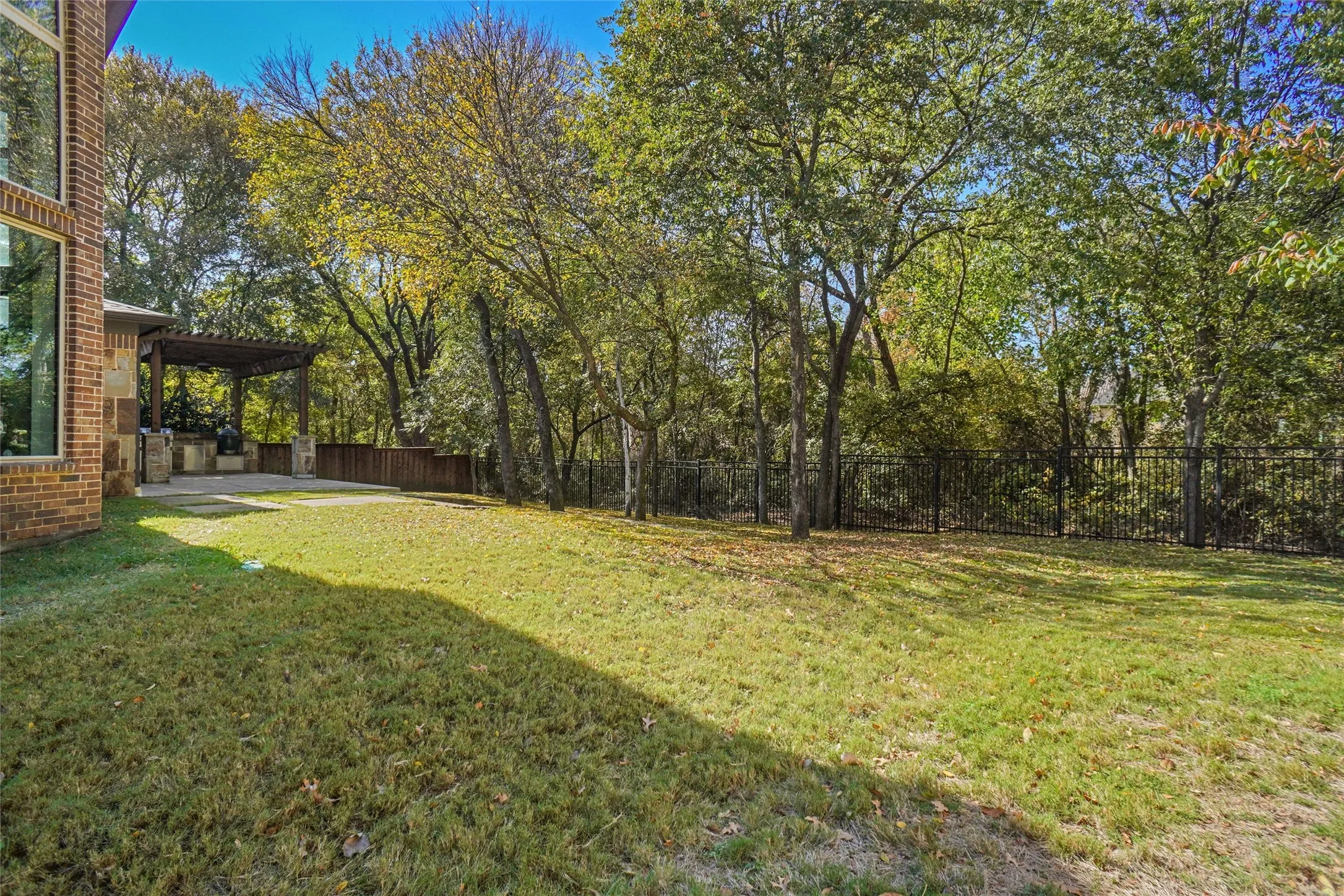 Expansive lawn area featuring a stone paver patio with a built-in outdoor kitchen under a wood pergola