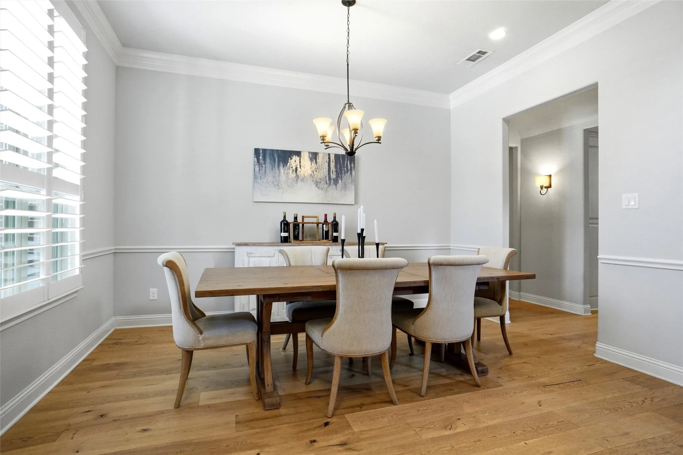 Dining area featuring wood-finish flooring, white plantation shutters, crown molding, and wainscoting