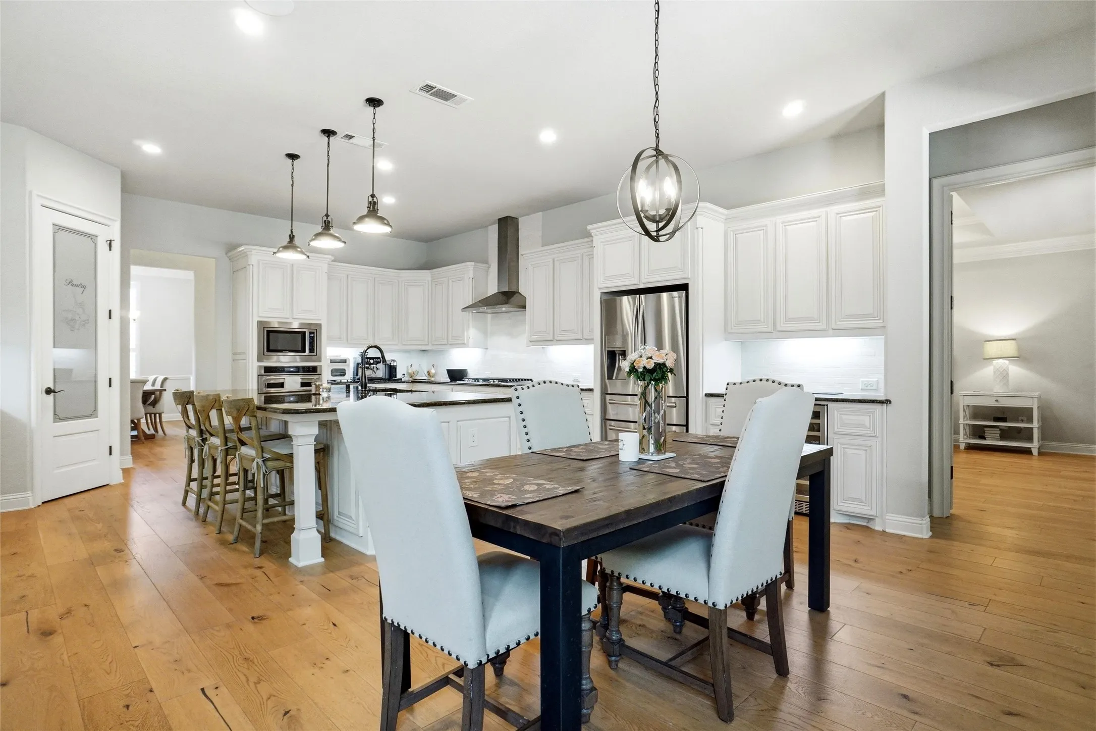 Gourmet kitchen featuring a central island with seating, stainless steel appliances, abundant white cabinetry, recessed lighting, and wood-finish flooring