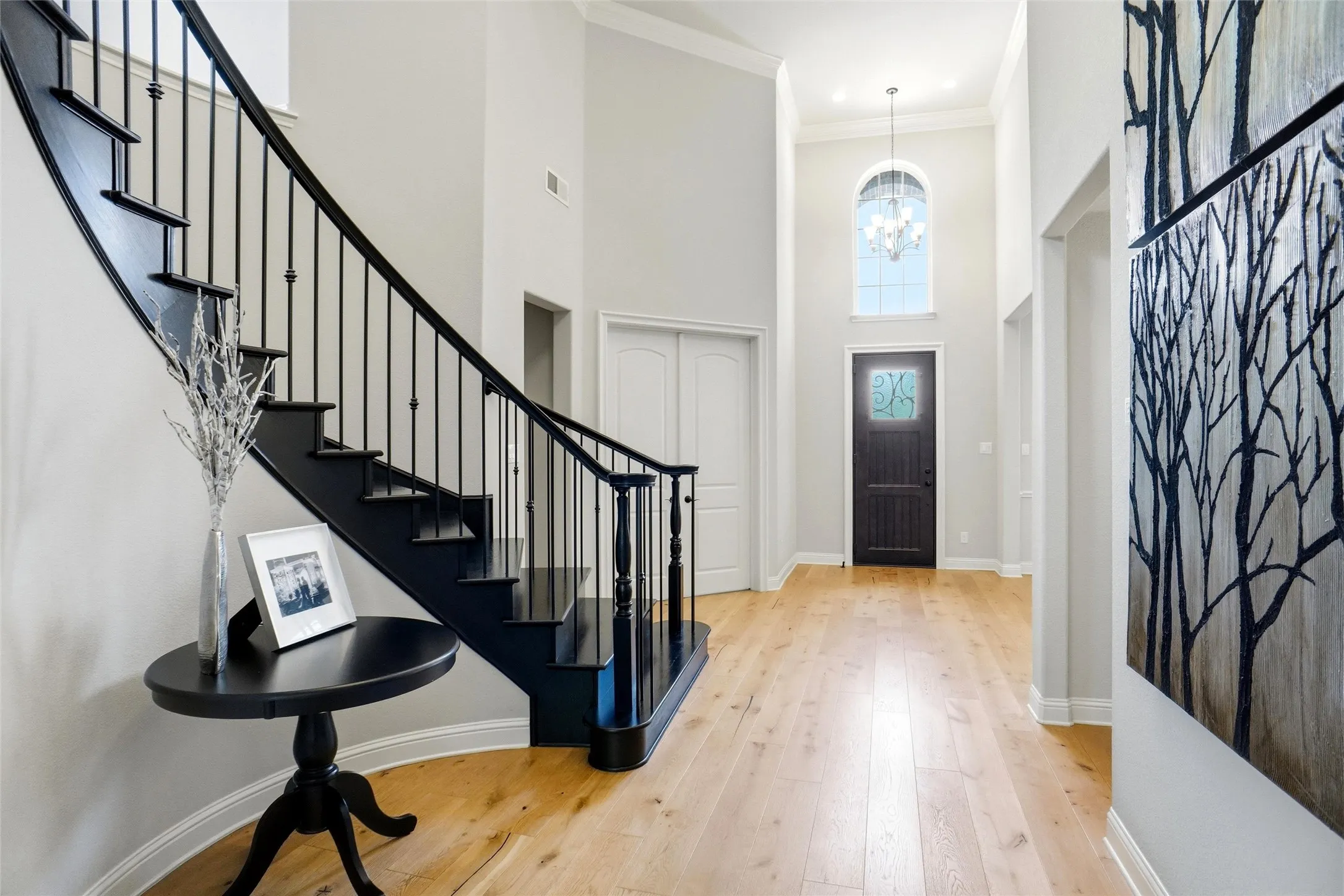 Two-story foyer featuring light wood-finish flooring, a dark wood entry door with an arched transom window, and a chandelier