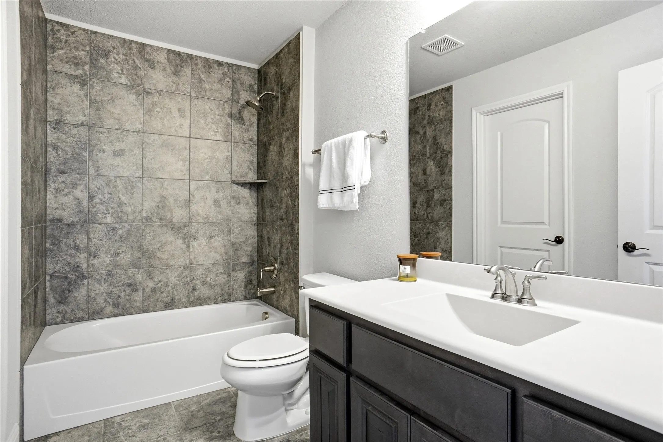 Bathroom featuring a white bathtub with a tiled shower surround, a built-in shower shelf, and coordinating floor tiles