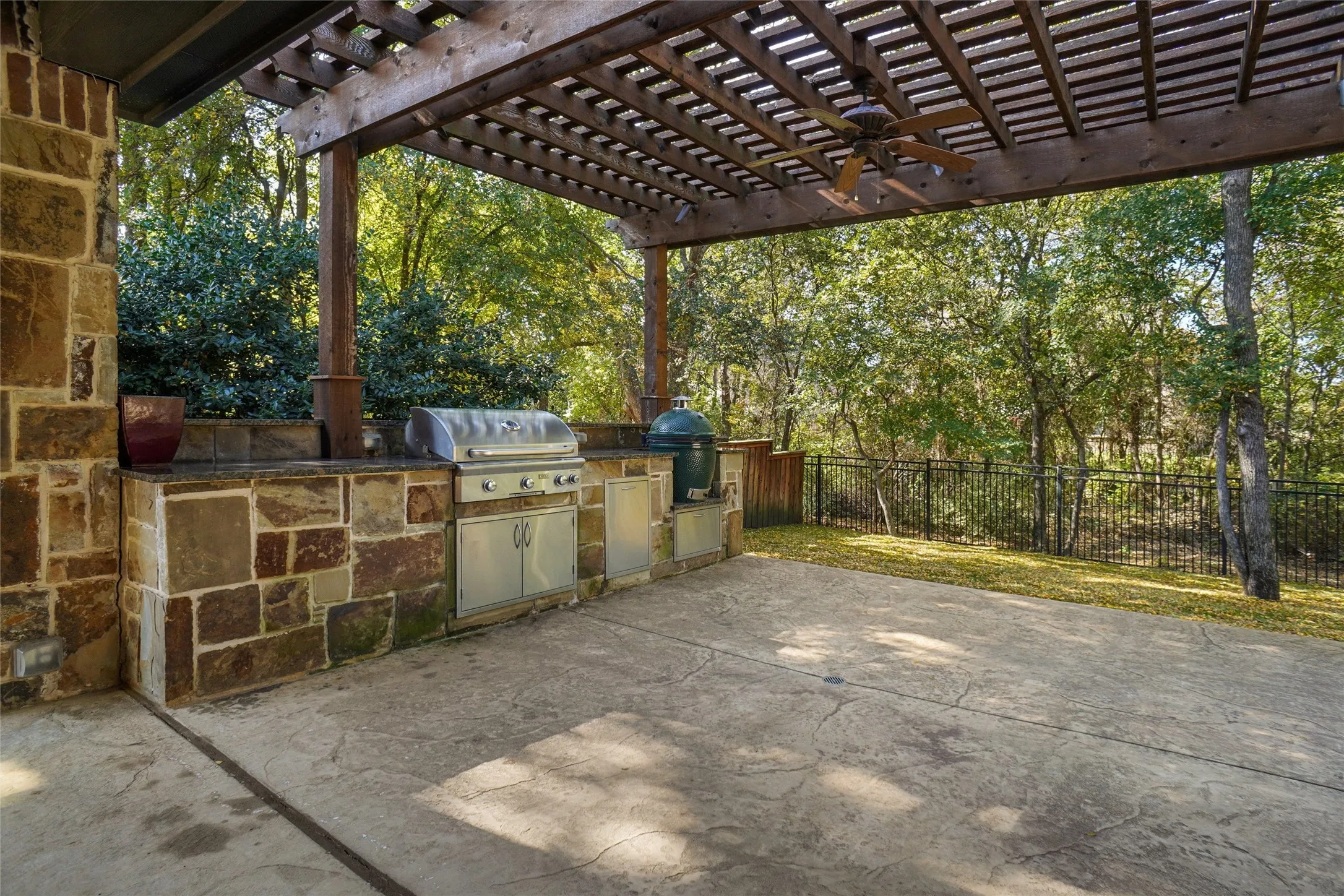 Covered patio featuring a wood pergola and ceiling fan, an outdoor kitchen with stone veneer base and built-in grill, and stamped concrete flooring