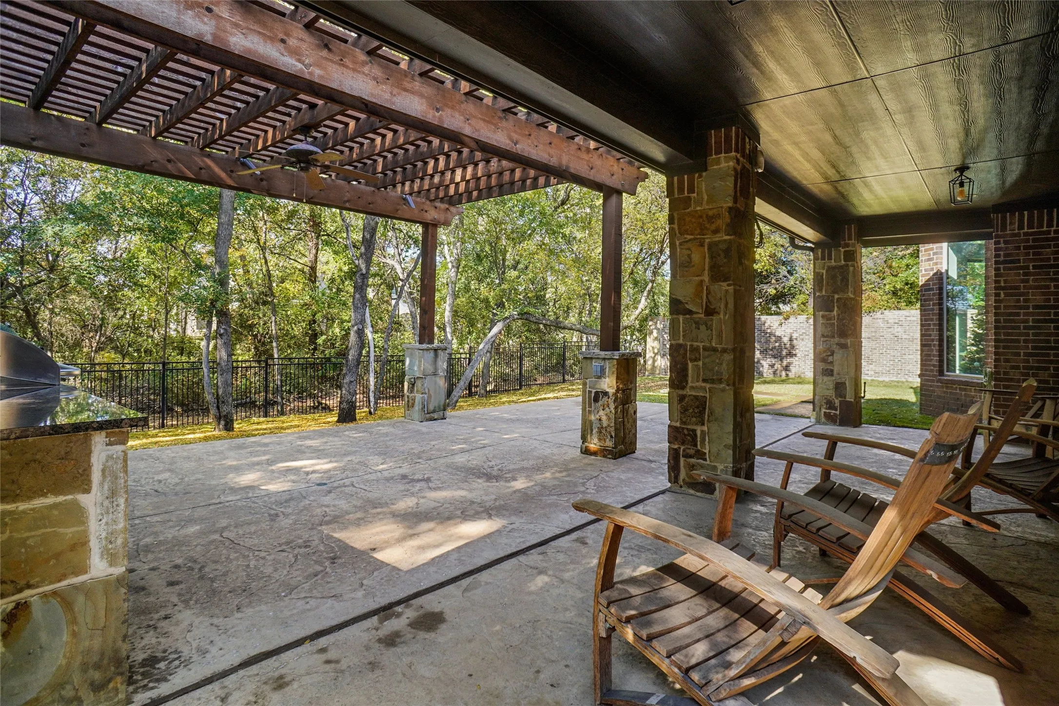 Expansive outdoor patio featuring a wood pergola, stone-clad columns, a built-in grill station with a dark countertop, and a wood-planked ceiling