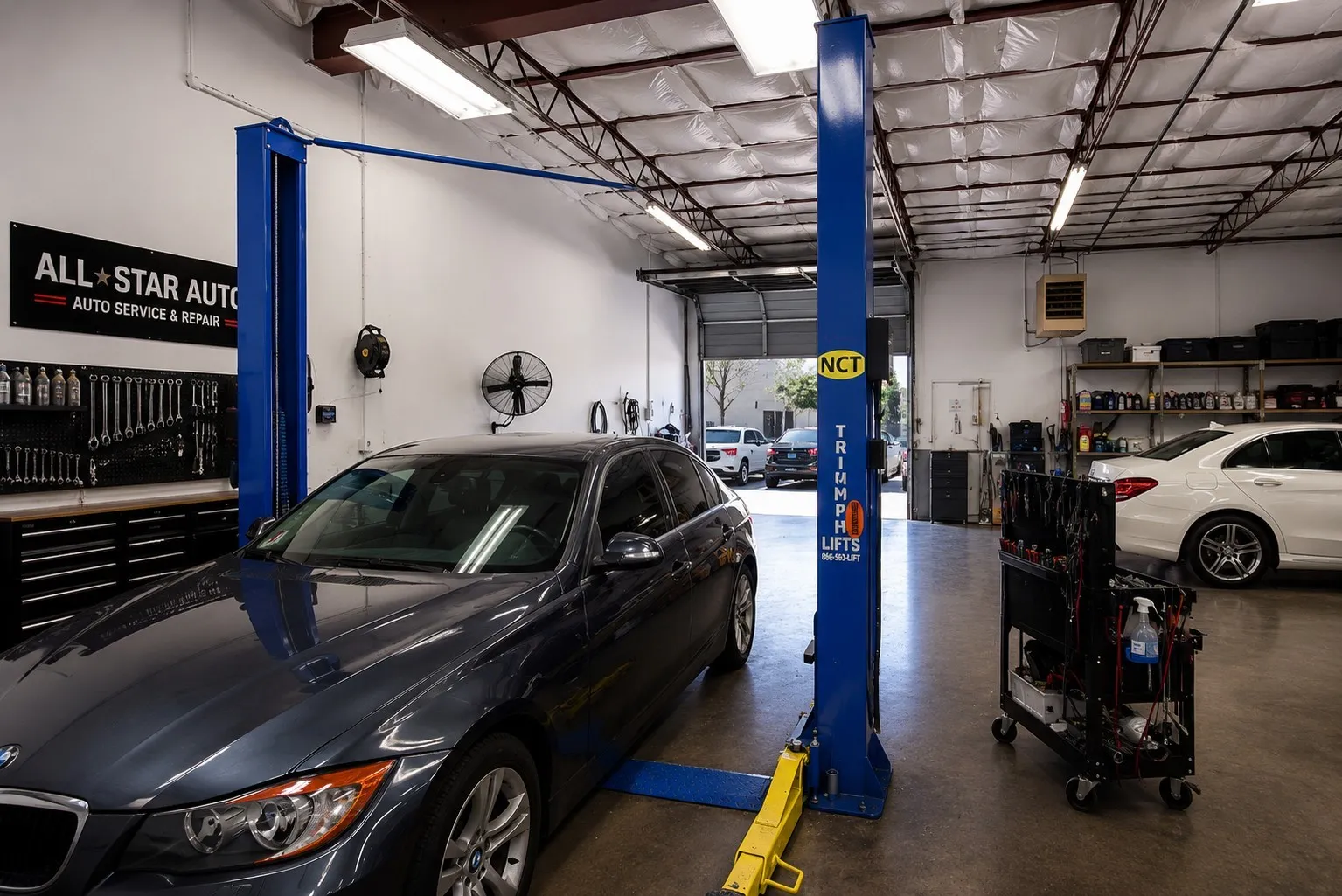 Automotive service bay with a vehicle lift, concrete flooring, and exposed ceiling trusses
