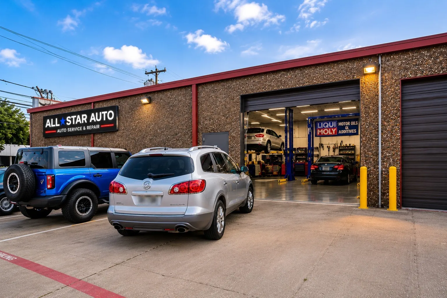 Commercial auto service building featuring a textured stone facade, a prominent illuminated business sign, and multiple roll-up garage doors