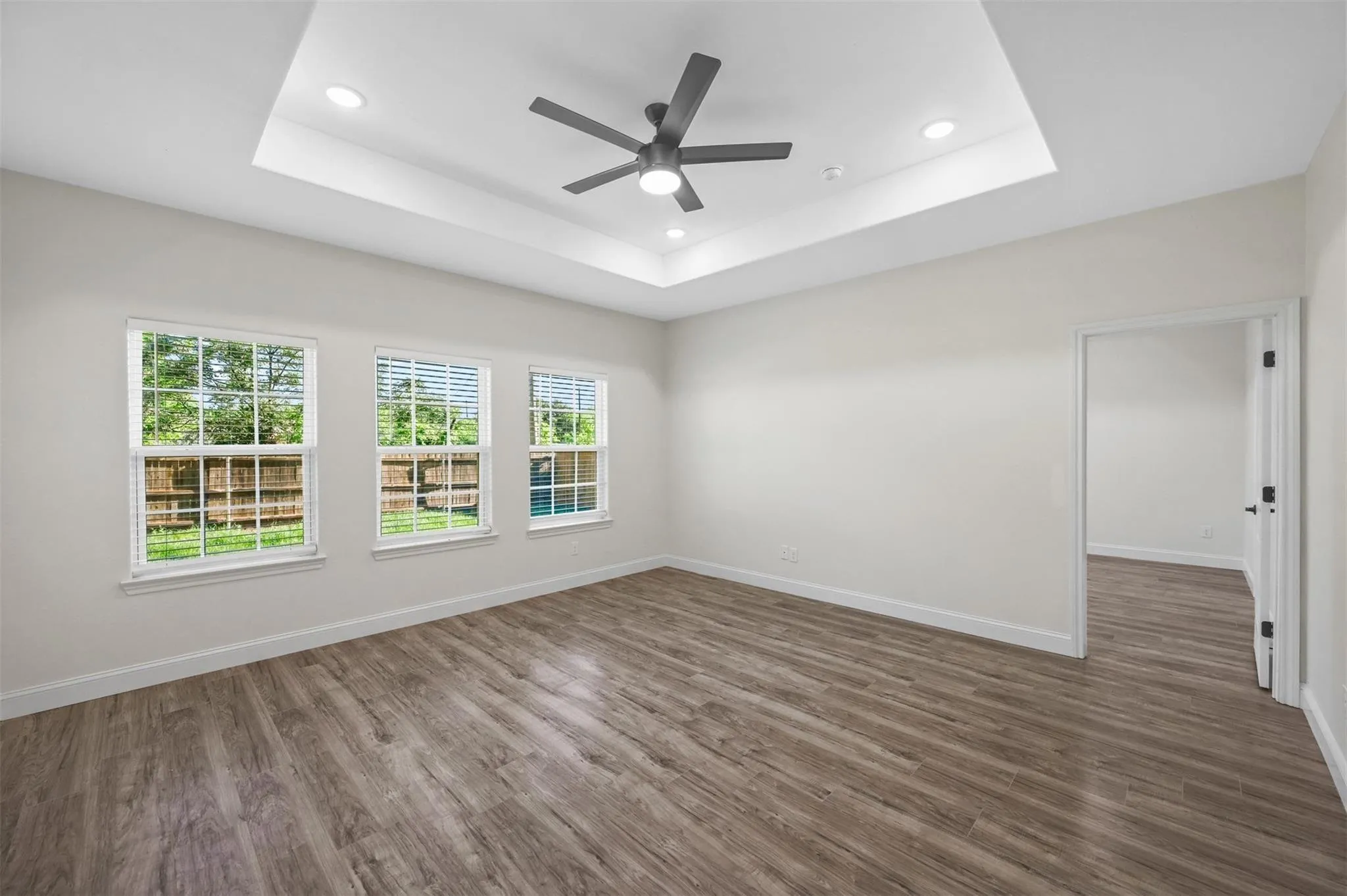 Spacious room featuring wood-finish flooring, a tray ceiling with recessed lighting, and a modern ceiling fan