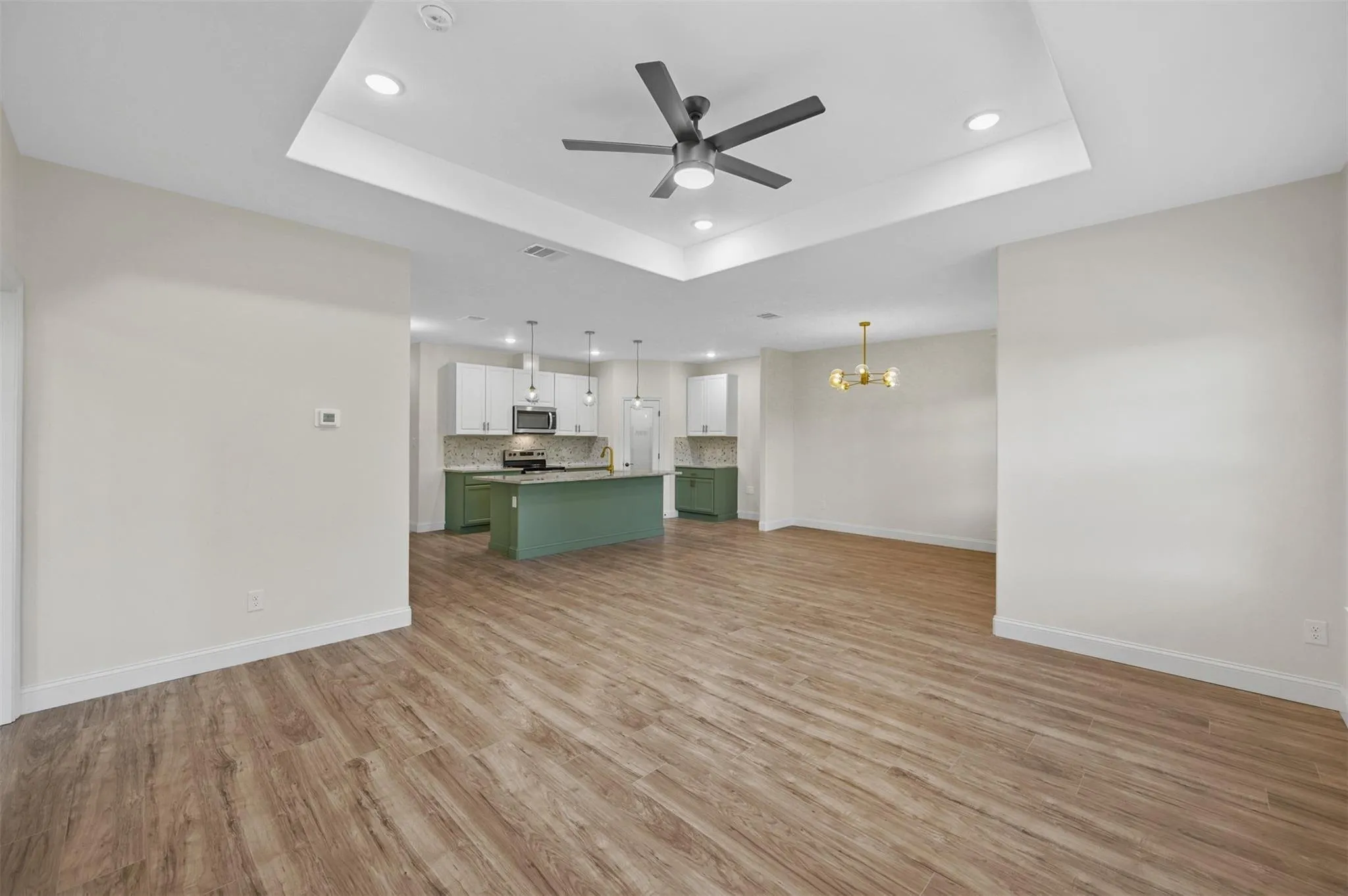 Spacious open-concept living area featuring wood-finish flooring, a tray ceiling with recessed lighting, and a contemporary ceiling fan