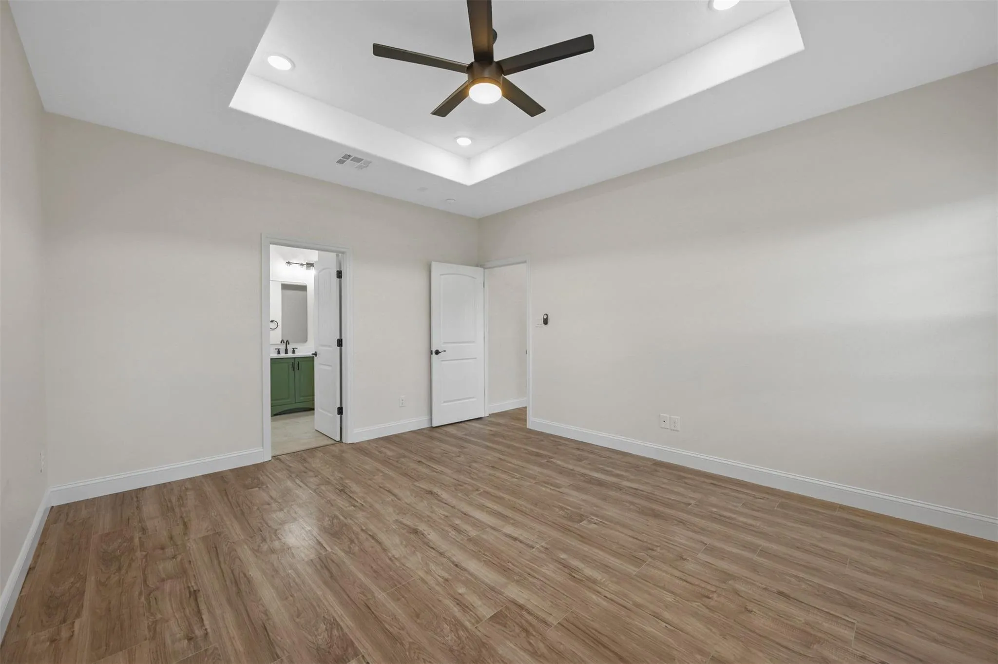 Spacious room featuring wood-finish flooring and a tray ceiling with recessed lighting