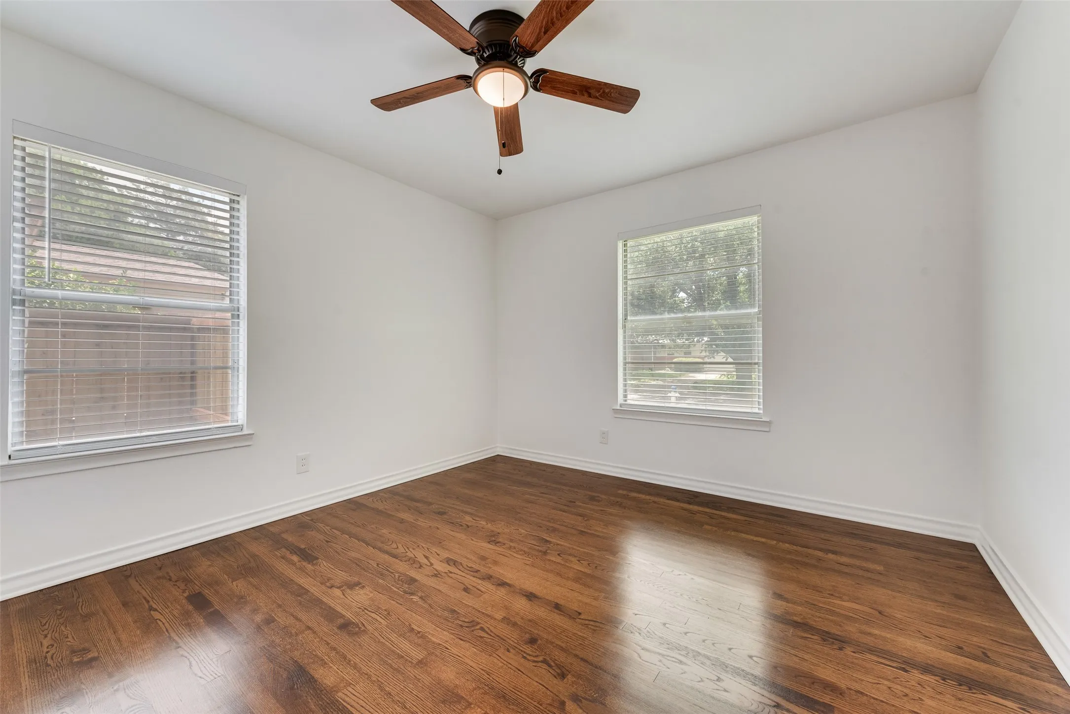 Room featuring rich wood-finish flooring, crisp white walls, and a ceiling fan with integrated lighting