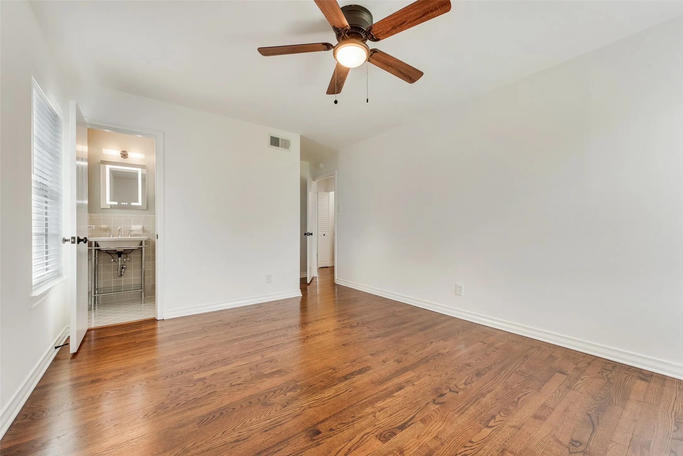 Spacious interior featuring rich wood flooring, crisp white walls, and a ceiling fan with integrated lighting
