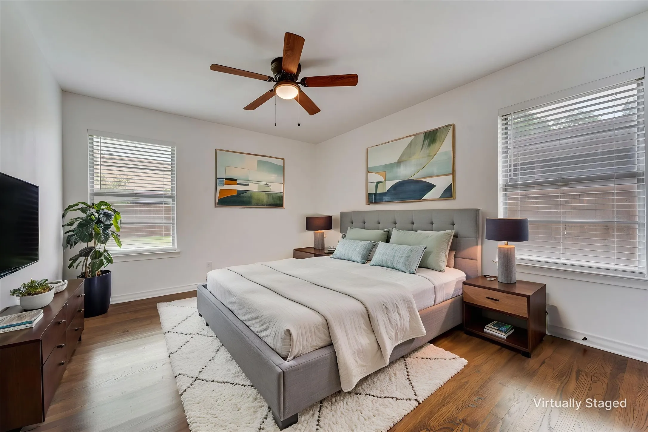 Bedroom featuring wood-finish flooring, white walls, and two windows with blinds