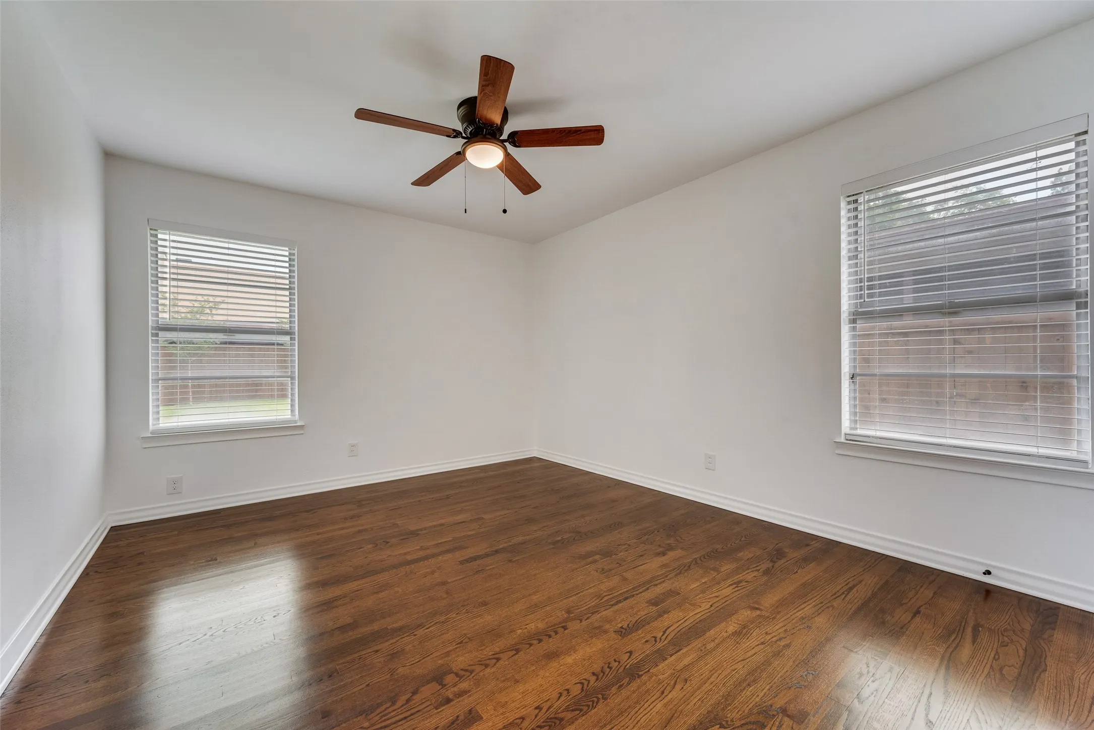 Room featuring wood-finish flooring, crisp white walls, and a ceiling fan with integrated lighting