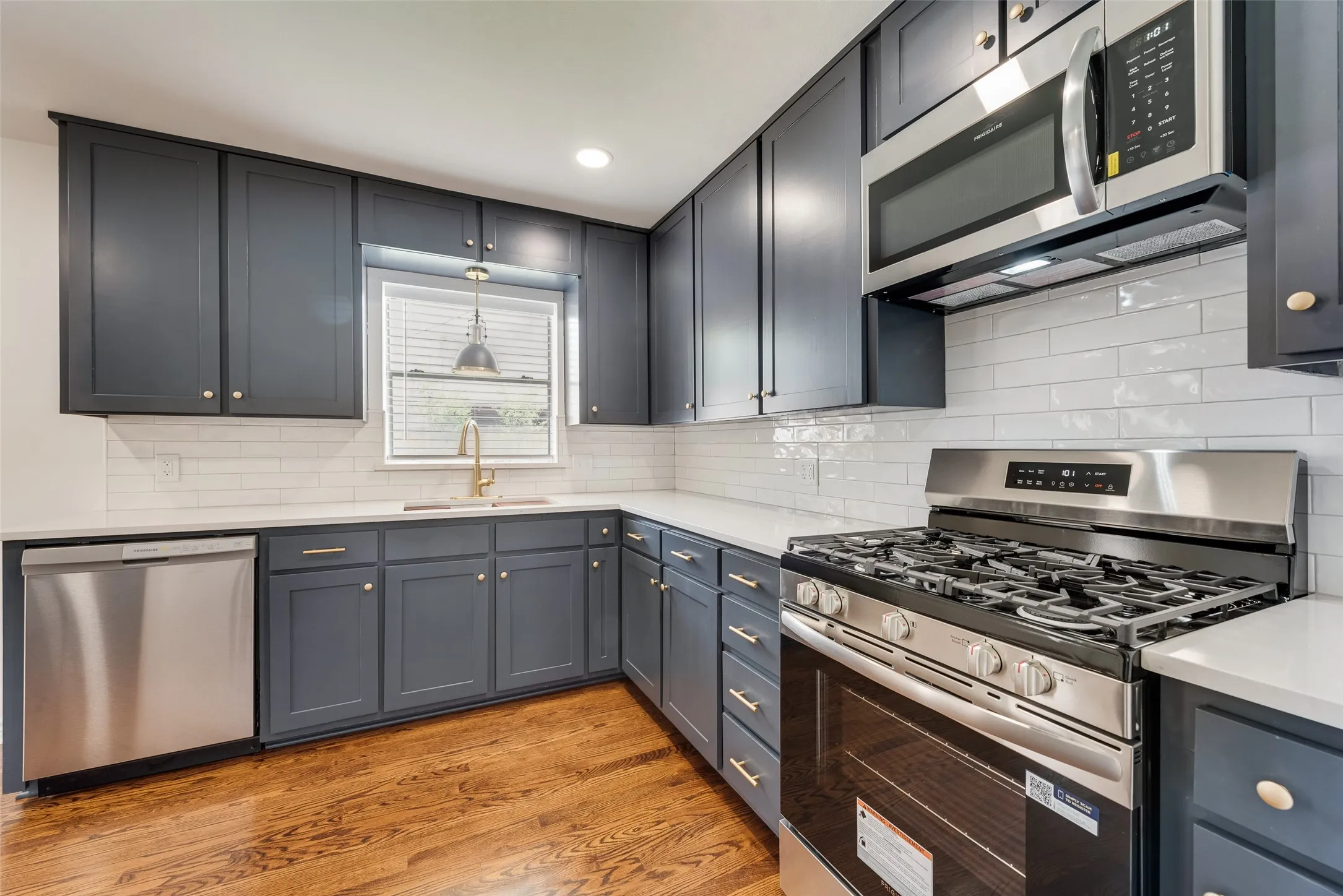 Kitchen featuring dark cabinetry, stainless steel appliances, a white subway tile backsplash, light countertops, and wood-finish flooring