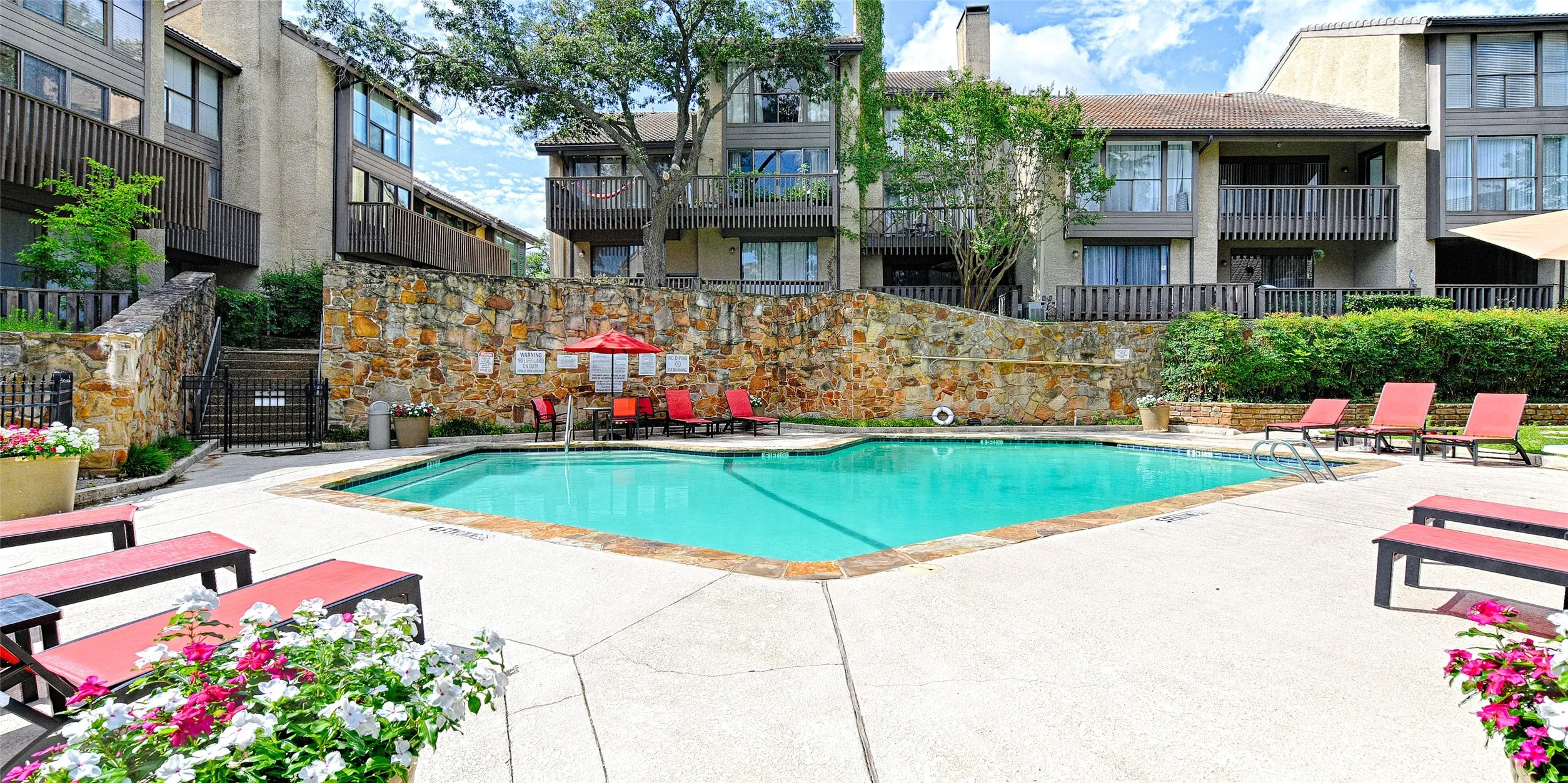 Inviting swimming pool with concrete decking, surrounded by natural stone retaining walls and lush landscaping