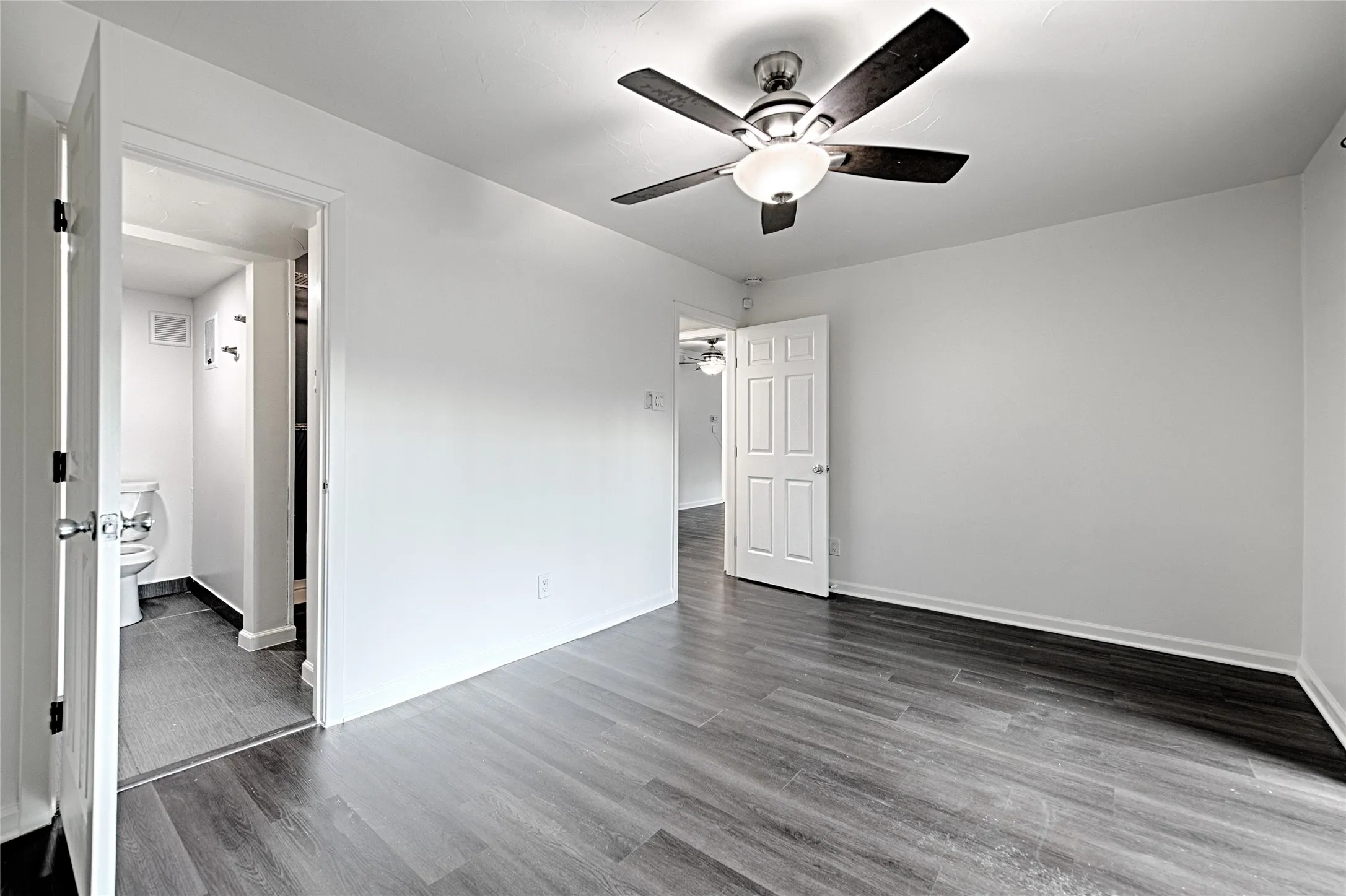 Spacious room featuring wood-finish flooring, white walls, and a ceiling fan with integrated lighting