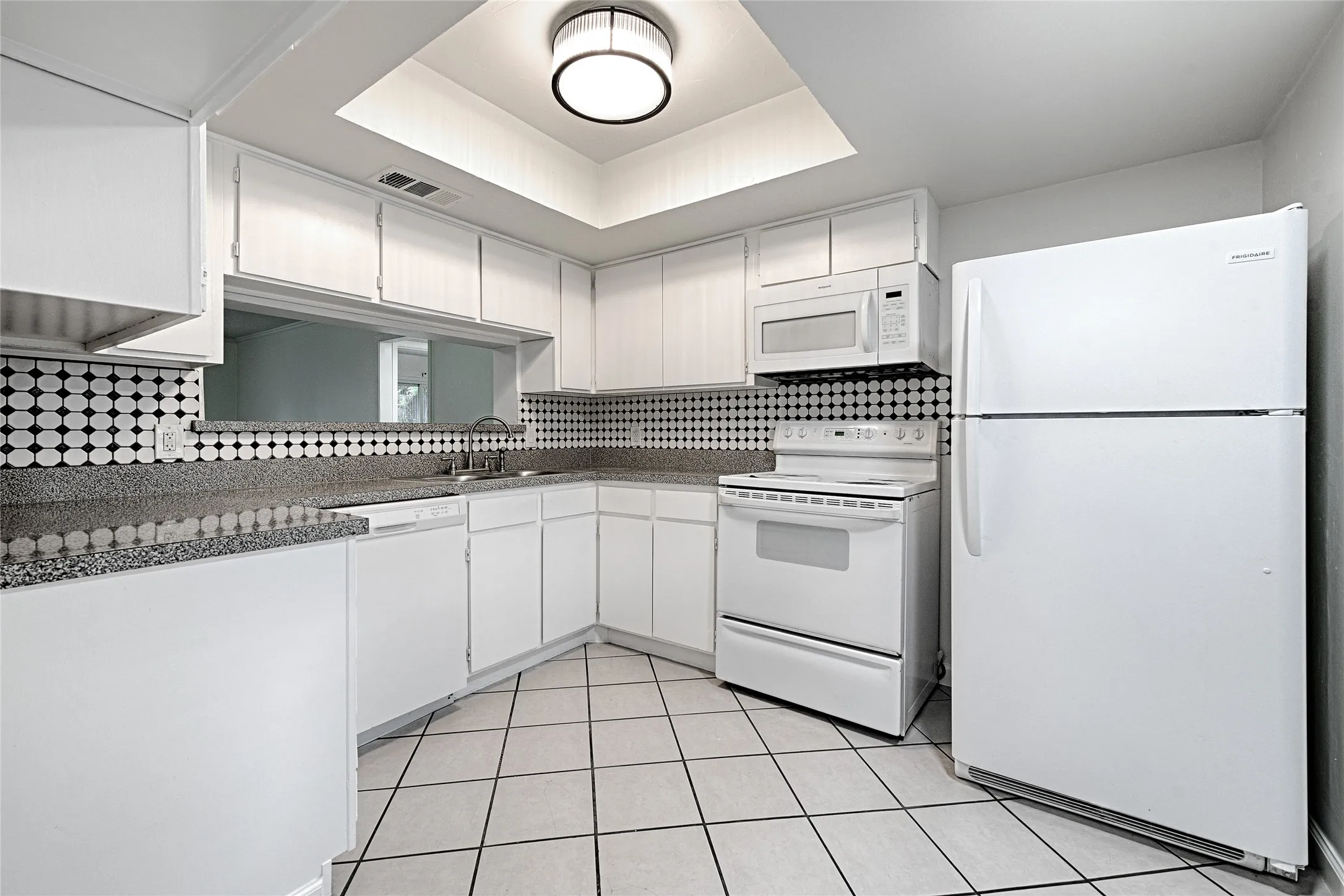 White kitchen featuring extensive cabinetry, tile flooring, granite-style countertops, and a full suite of white appliances including a refrigerator, range, microwave, and dishwasher
