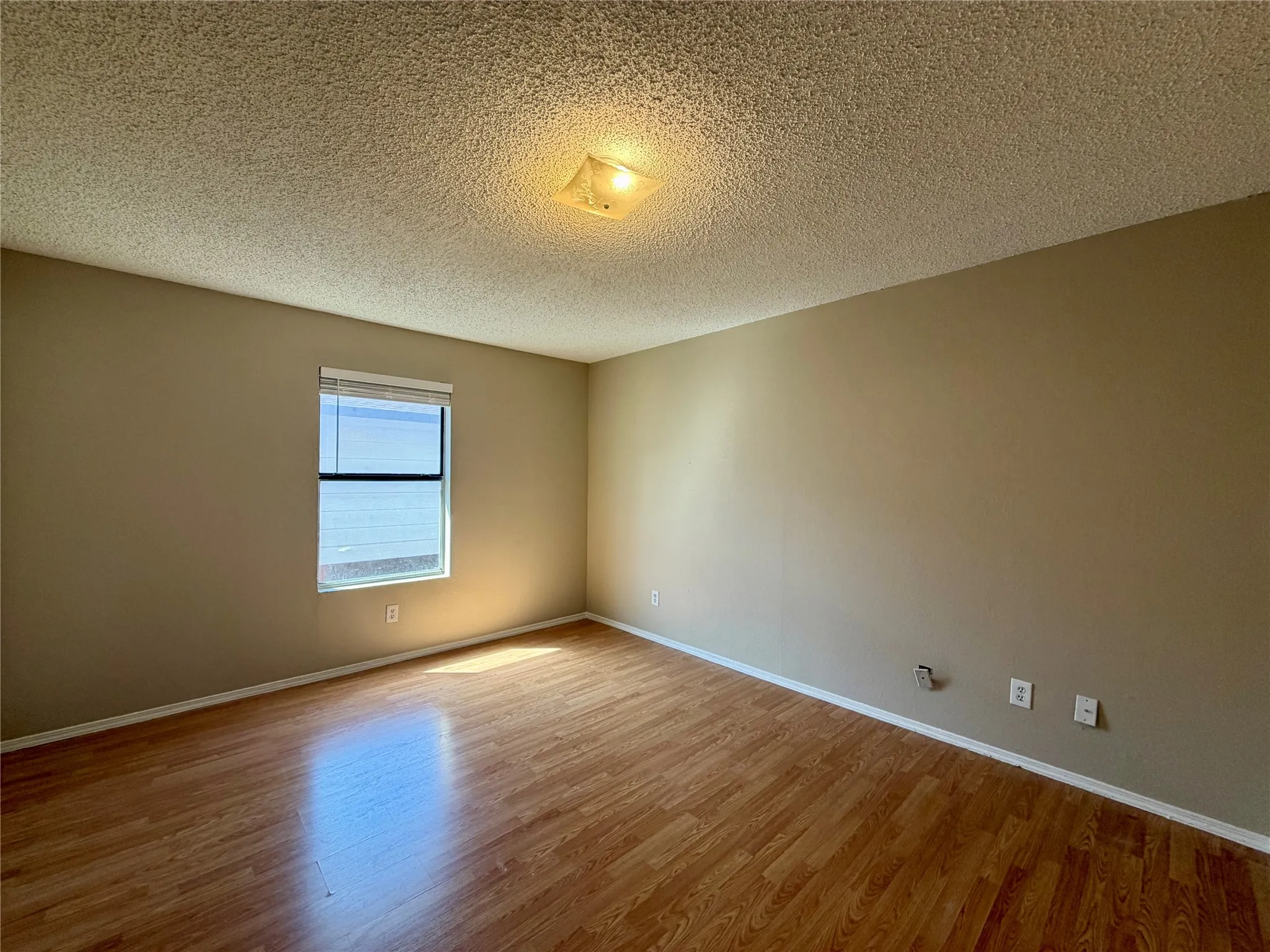 Wood-finish flooring with a window featuring blinds, textured ceiling, and neutral wall tones