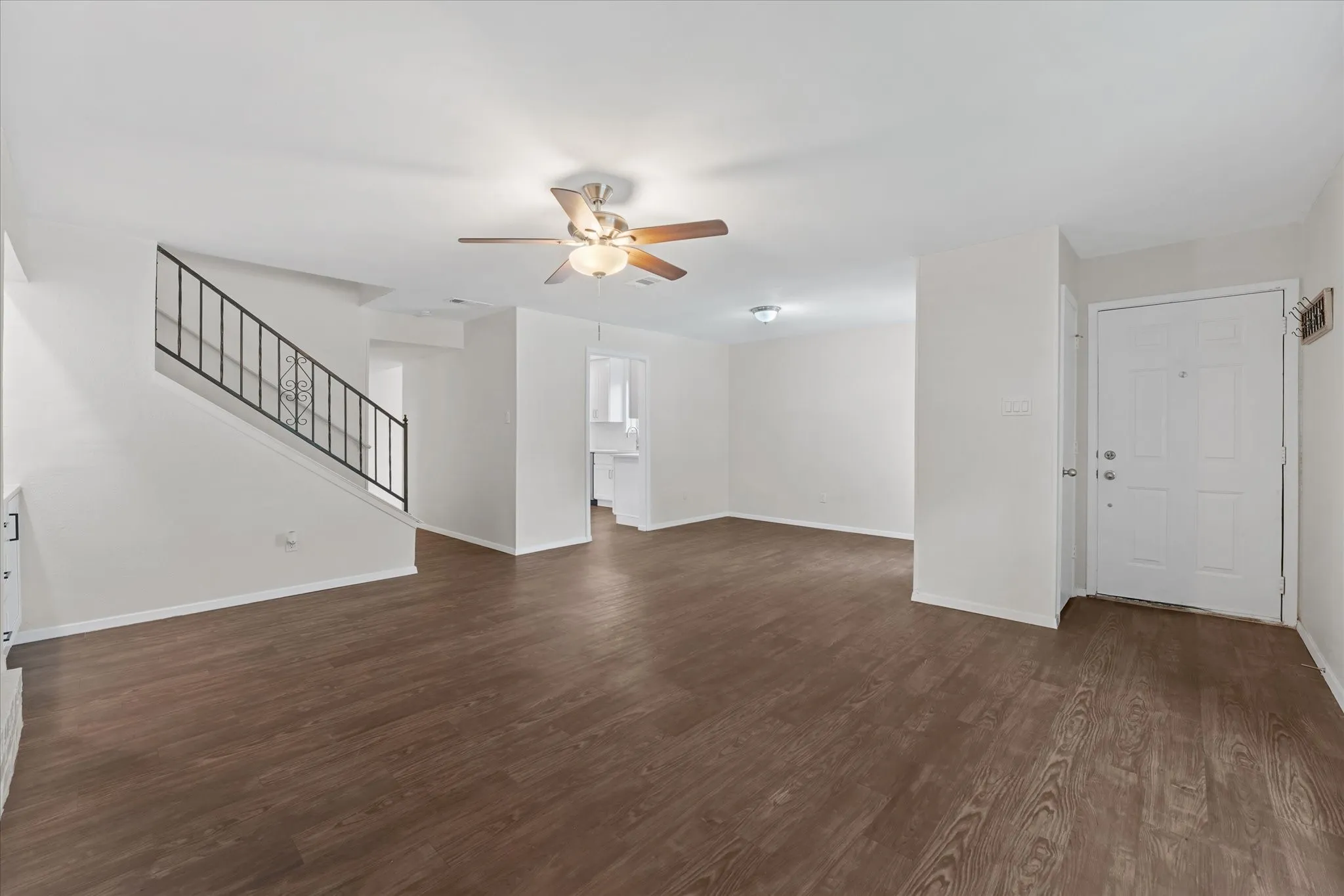 Spacious living area featuring wood-finish flooring, a ceiling fan with integrated lighting, and a white paneled entry door
