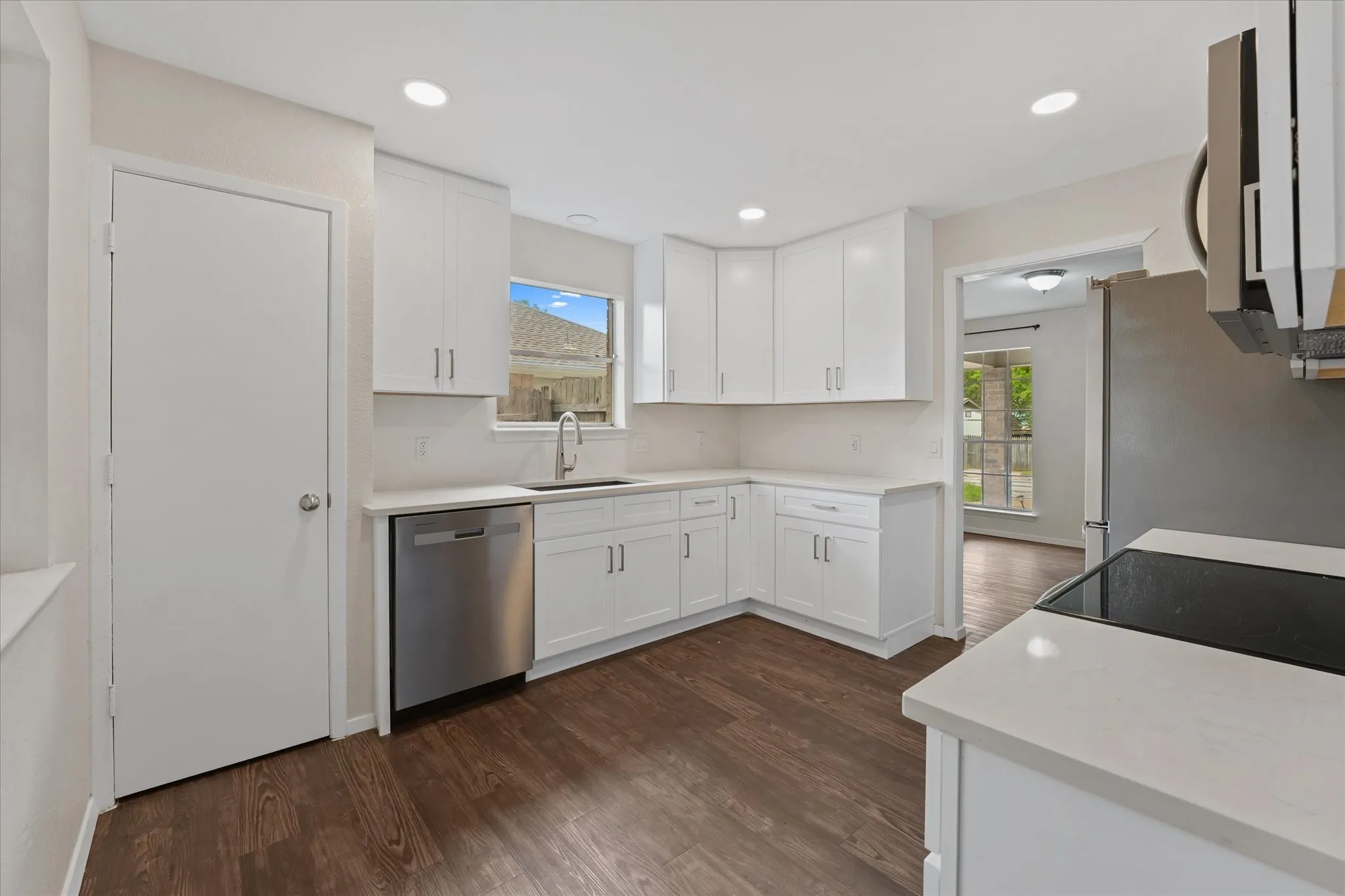 Kitchen featuring white shaker cabinetry, light-toned countertops, stainless steel appliances, dark wood-finish flooring, and recessed lighting