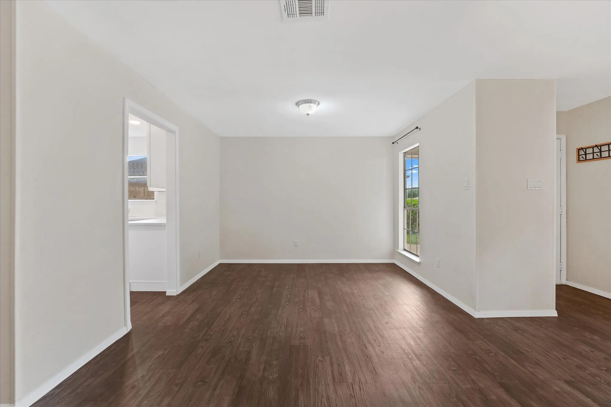 Spacious room featuring wood-finish flooring, light-toned walls, a large window, a ceiling-mounted light fixture, and white baseboards