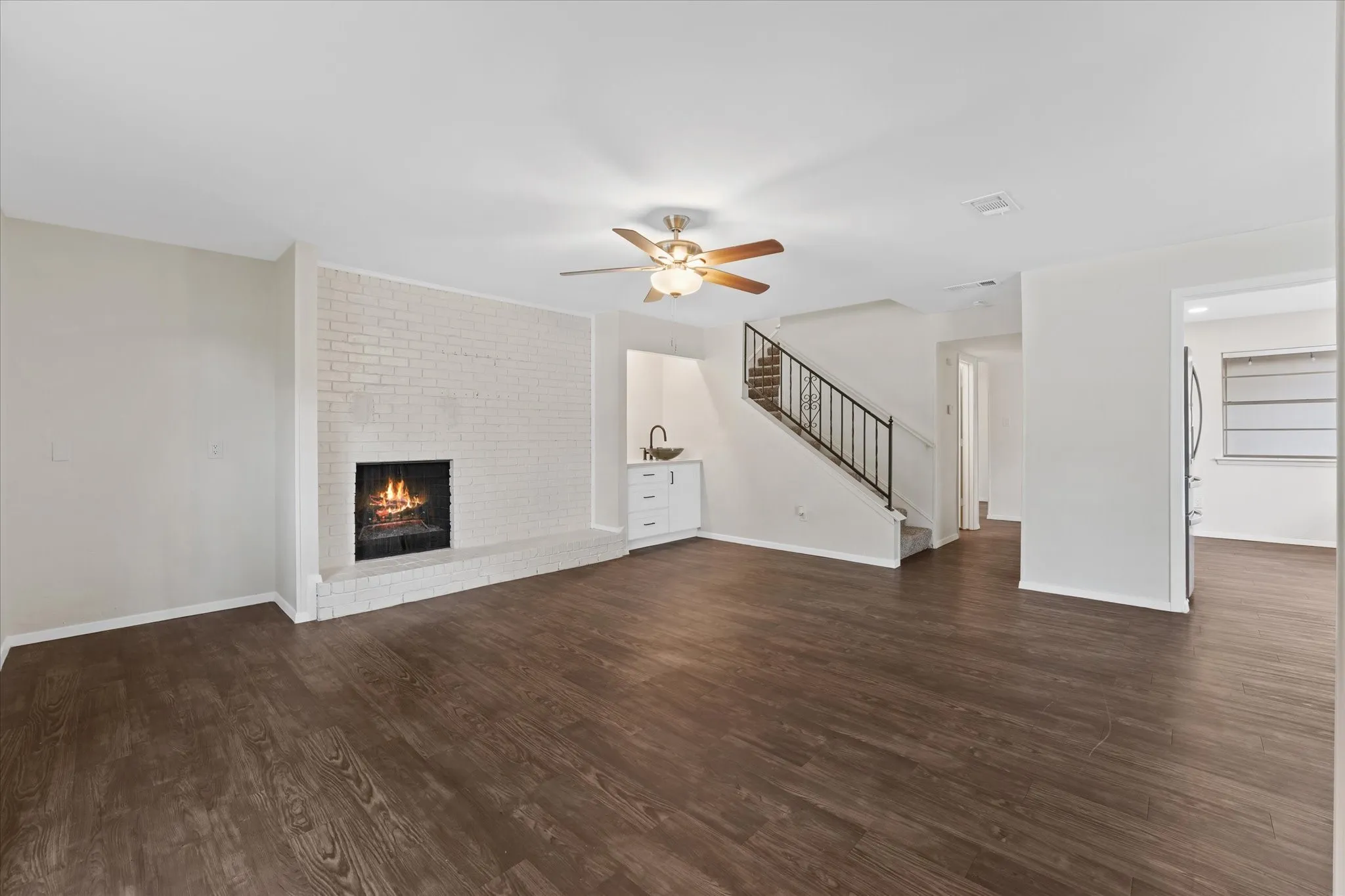 Spacious living area featuring wood-finish flooring, a white brick fireplace, and a built-in wet bar with white cabinetry
