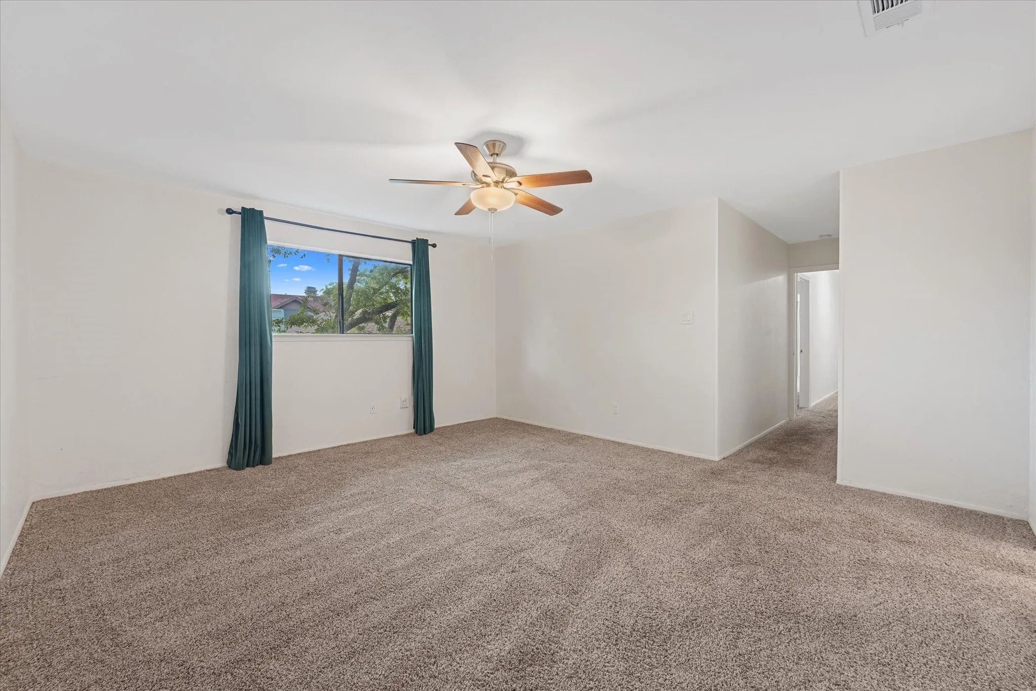 Spacious room featuring neutral carpet flooring, light-toned walls, a ceiling fan with integrated lighting, and a large window providing natural light