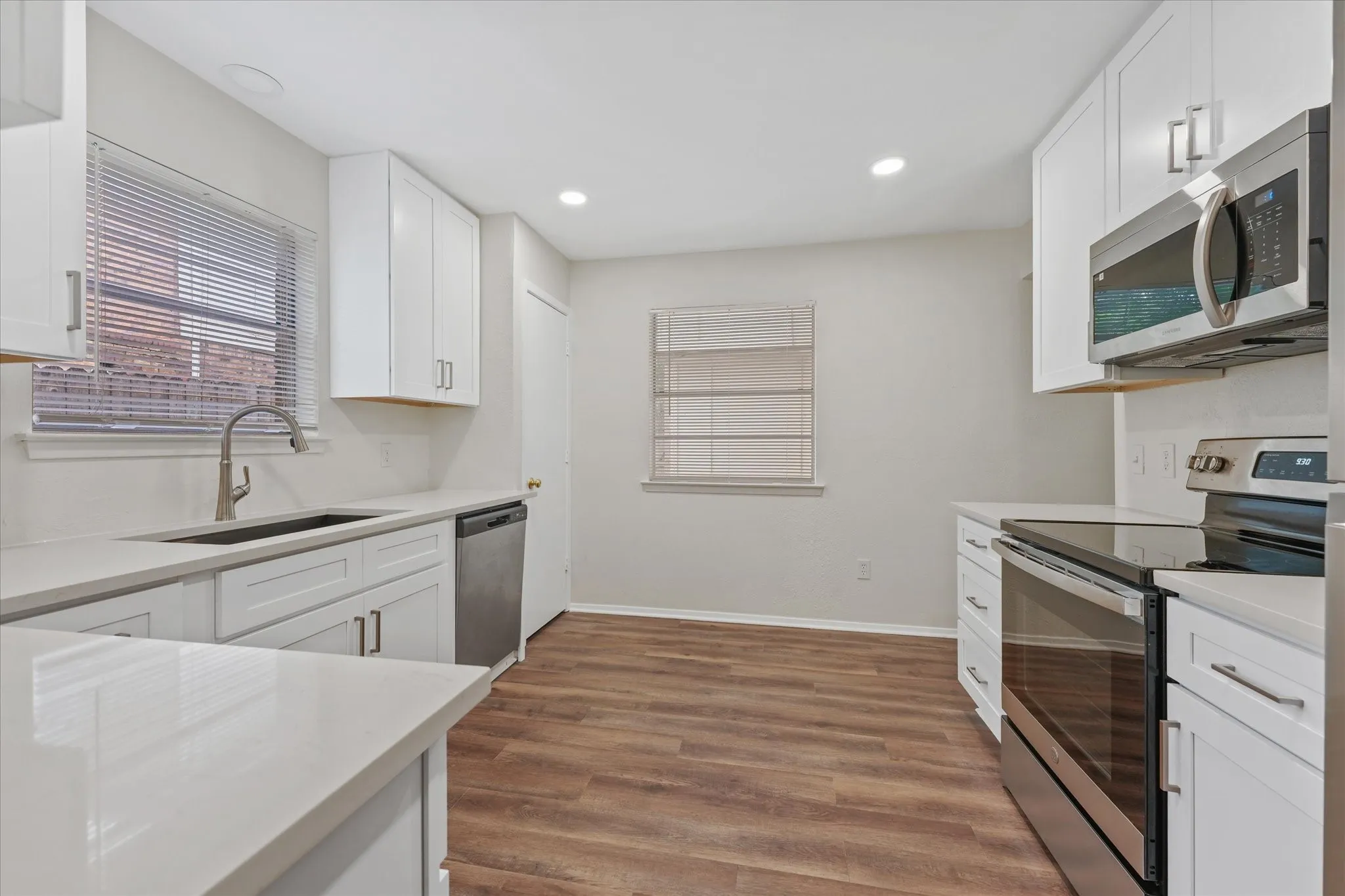 Modern kitchen featuring white shaker cabinetry, light-toned countertops, and wood-finish flooring