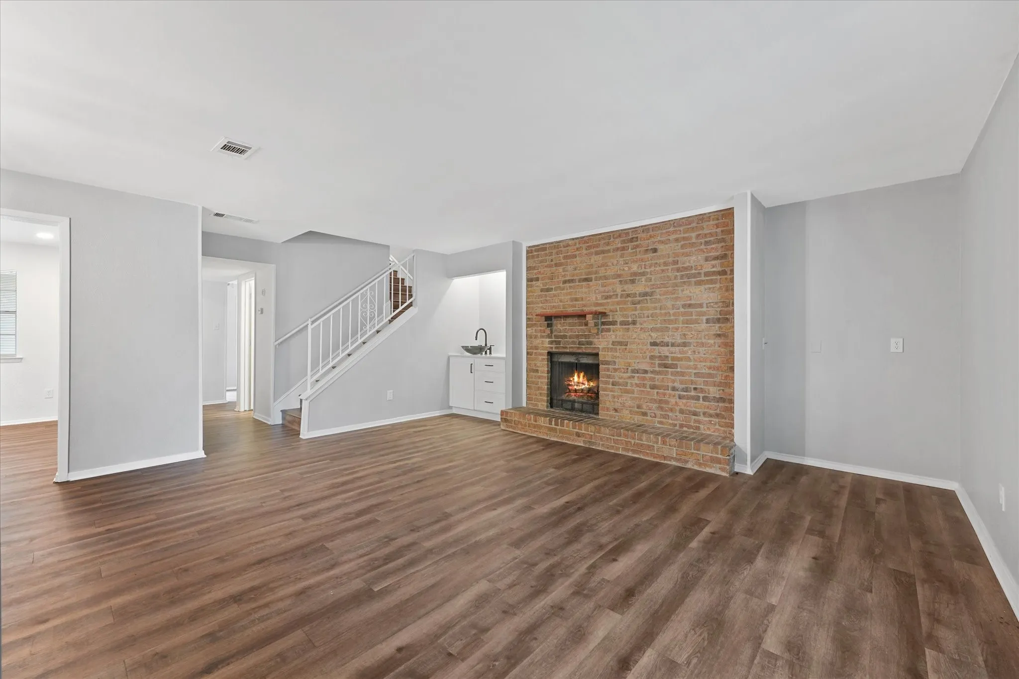 Spacious living area featuring wood-finish flooring, a brick fireplace with a wood mantle, and a built-in wet bar with white cabinetry