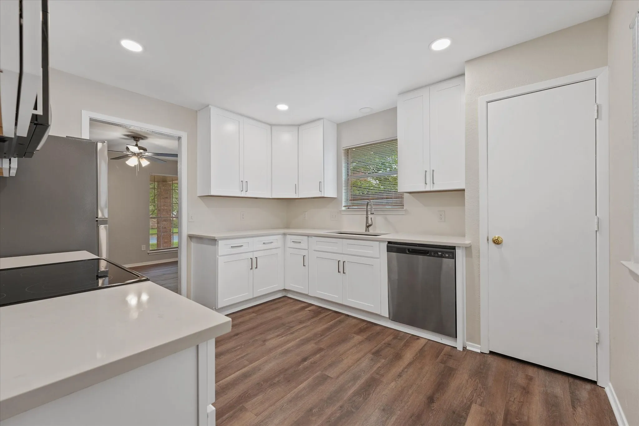 Kitchen featuring wood-finish flooring, white cabinetry with silver-tone hardware, light-toned countertops, a stainless steel dishwasher, and a window above the sink