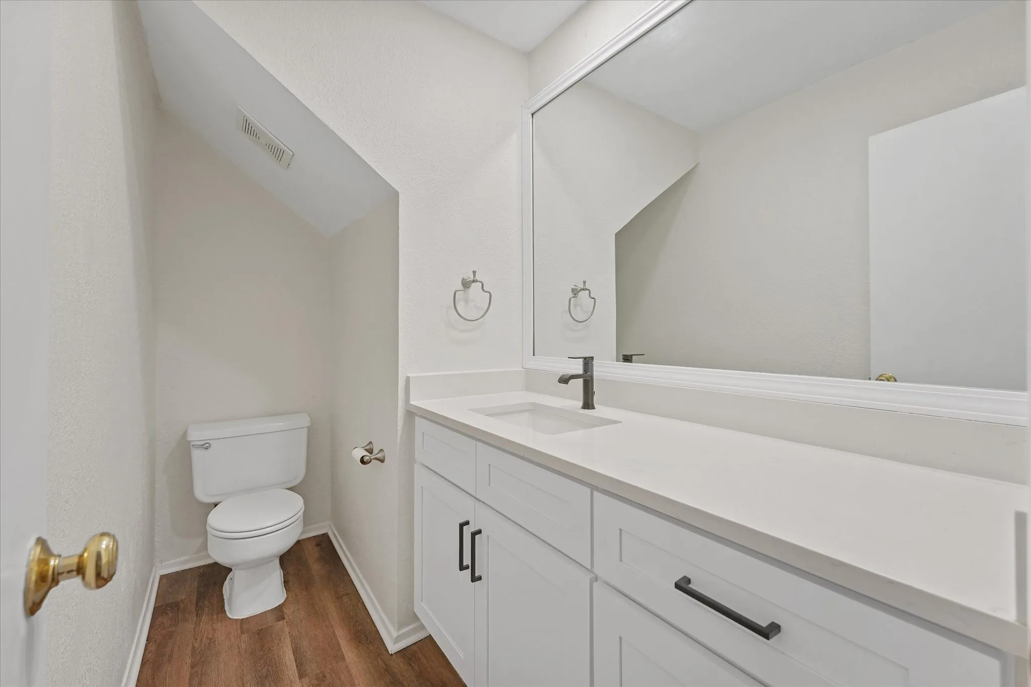 Downstairs powder room featuring a white single vanity with a solid surface countertop, matte black faucet, and coordinating cabinet hardware